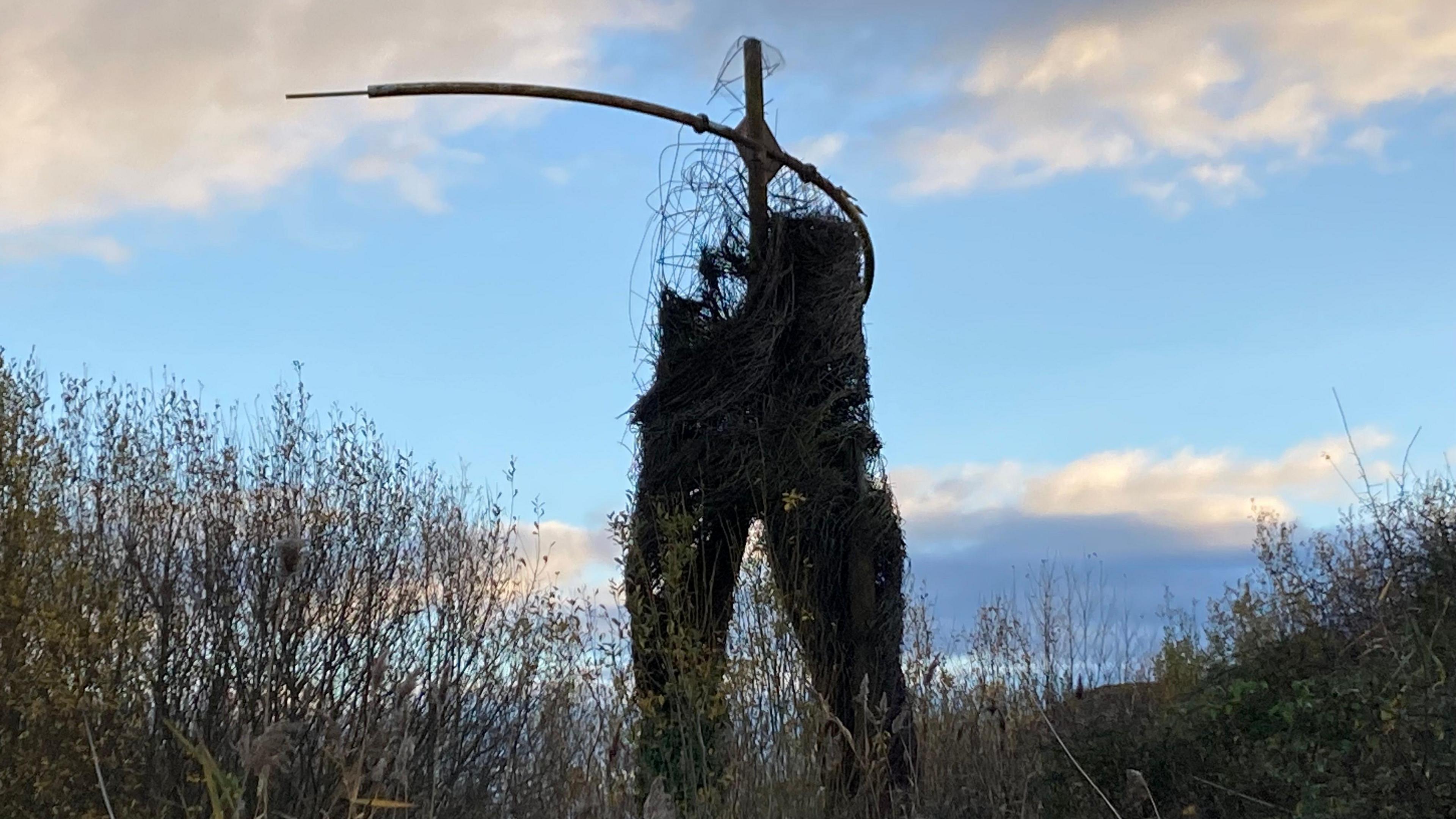 The lower half of a giant willow structure, with the upper half a broken down wire mesh and frame