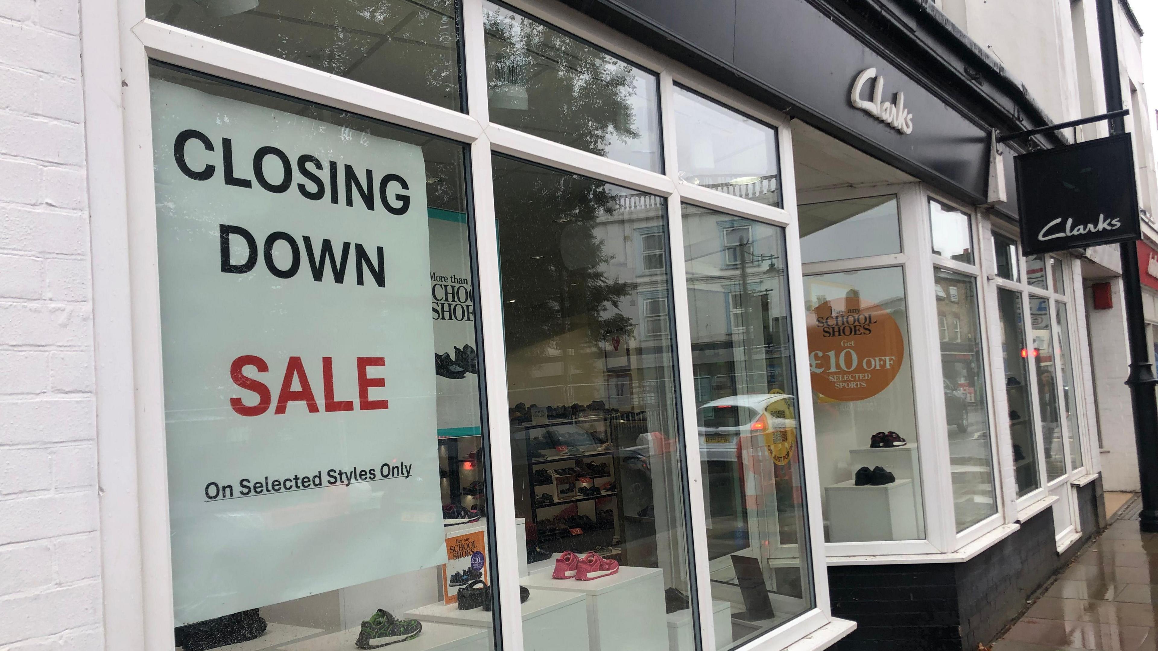 Photo of a Clarks storefront taken from outside the shop on the high street. It has shoes on display in the windows and a 'closing down sale' sign.