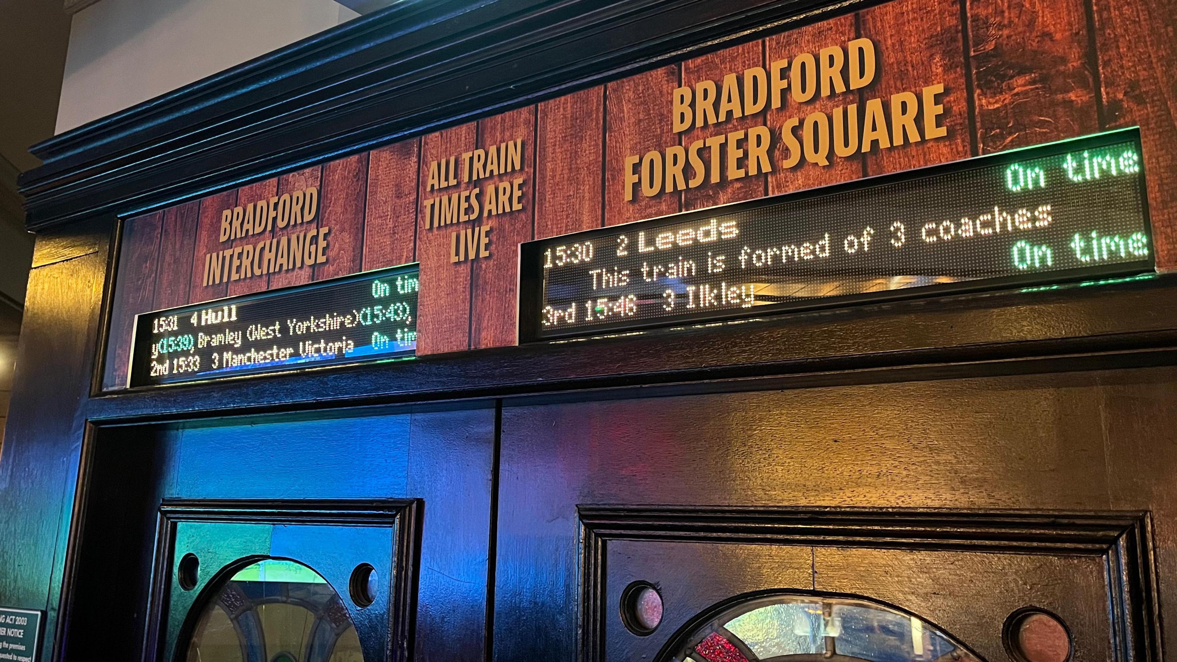 Digital train displays above a pair of pub doors with the names of the relevant local stations above them