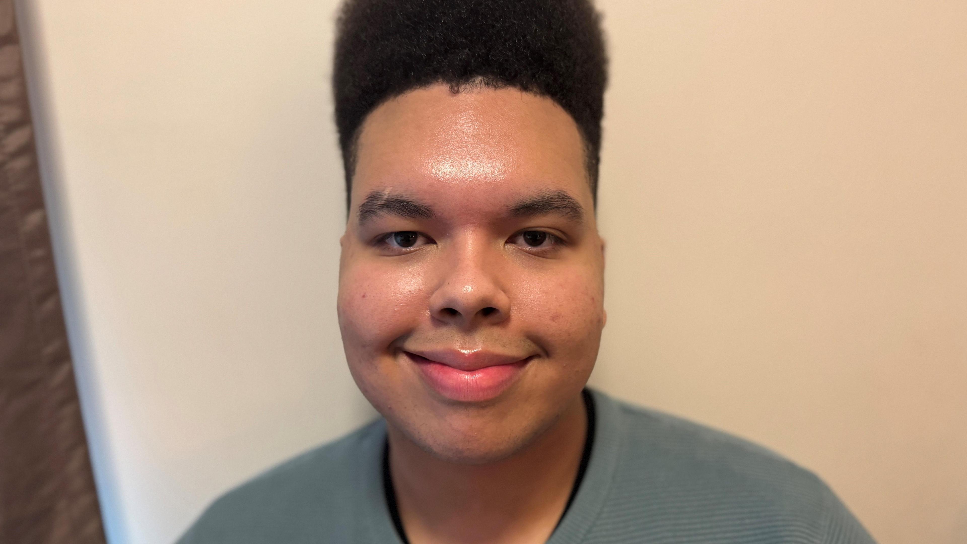 A smiling black man with very tall hair and a blue tshirt in front of a white background