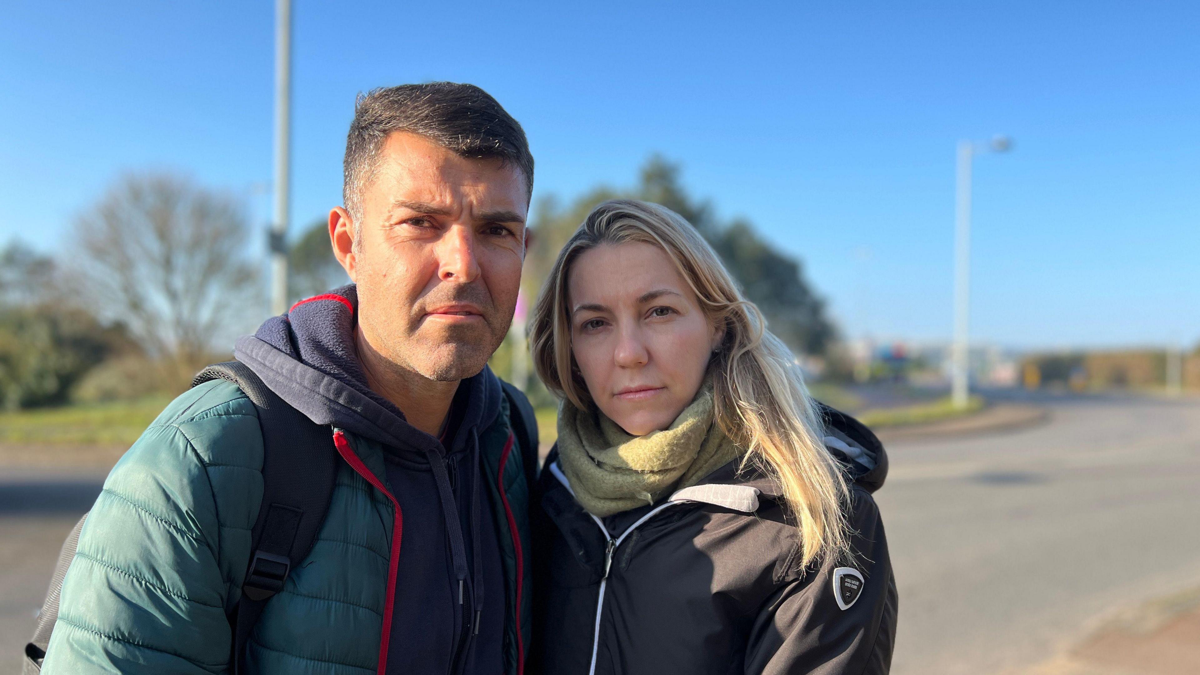 Victoria Ruellan and Jonathan Rodriguez wearing coats and scarves look at the camera but they aren't smiling