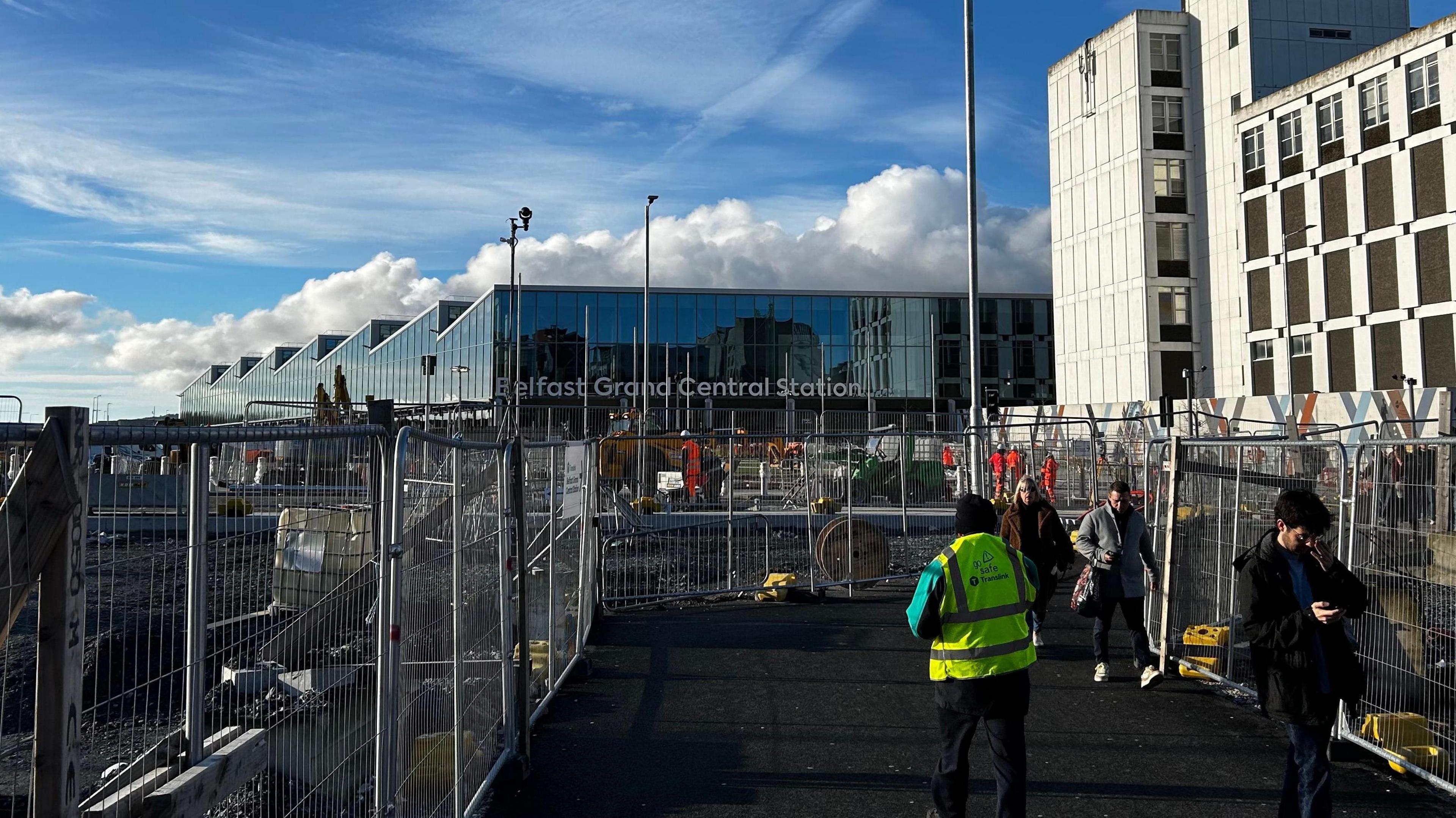 A picture of Belfast Grand Central Station, a large glass transport hub, from the view of a walkway which goes through ongoing building work.