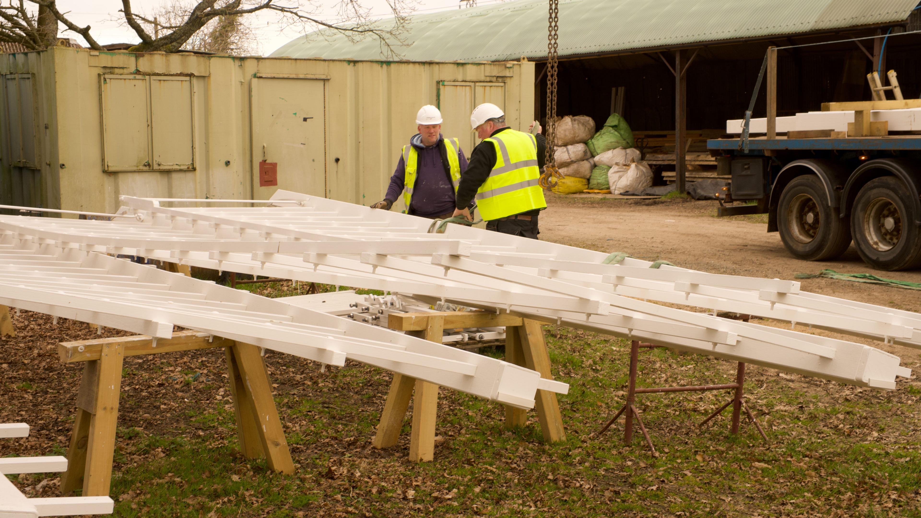 Two men wearing high-vis jackets and white hard hats prepare the sails to be lifted on to a lorry.