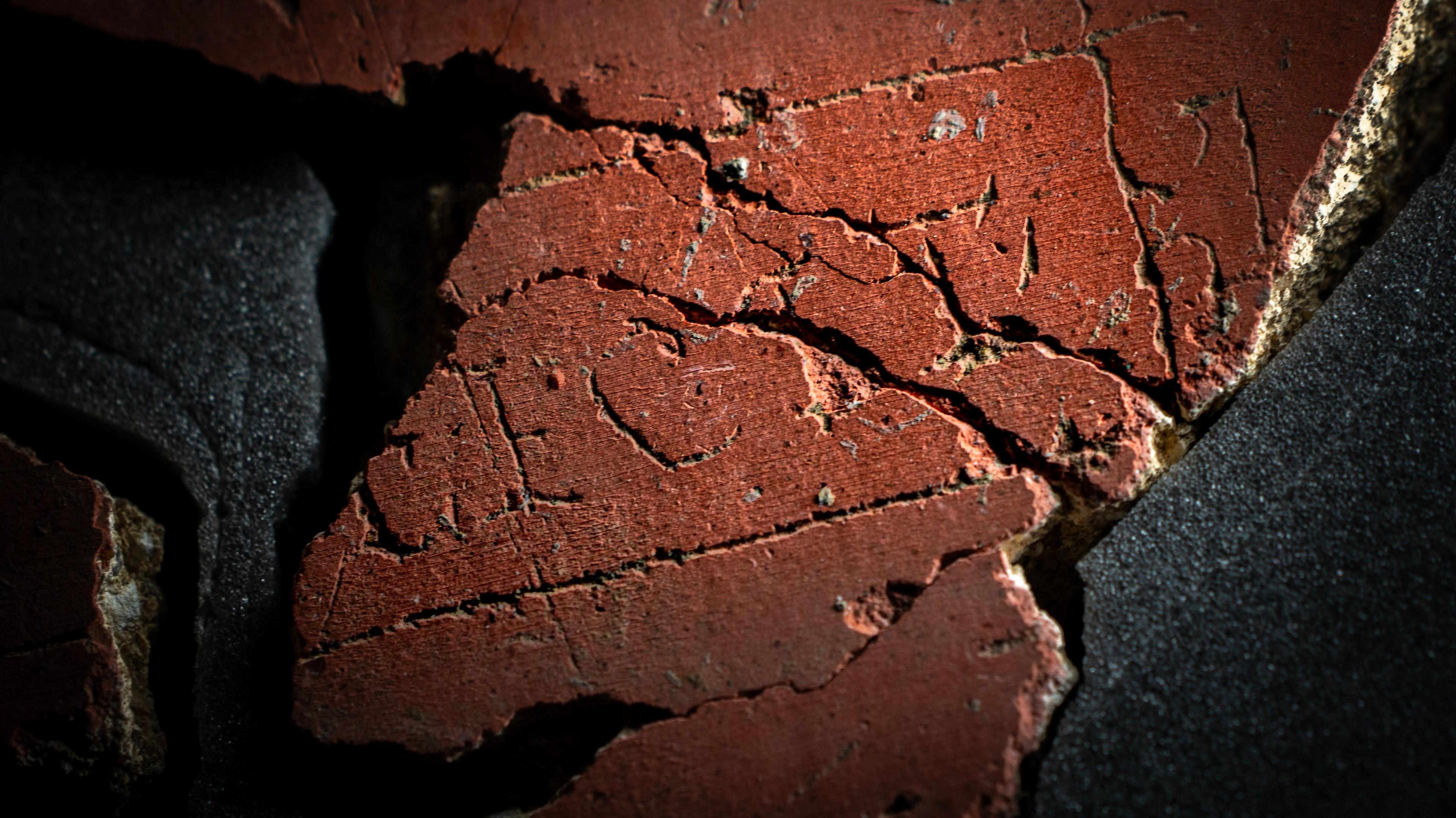 A close up of piece of red plaster, made up of several smaller pieces, with the letters F E C I T in capitals clearly visible with a line drawn in a square around three sides of the word. The left hand side of the plaster, where the name of the person or group who made the piece of art should be, is missing.