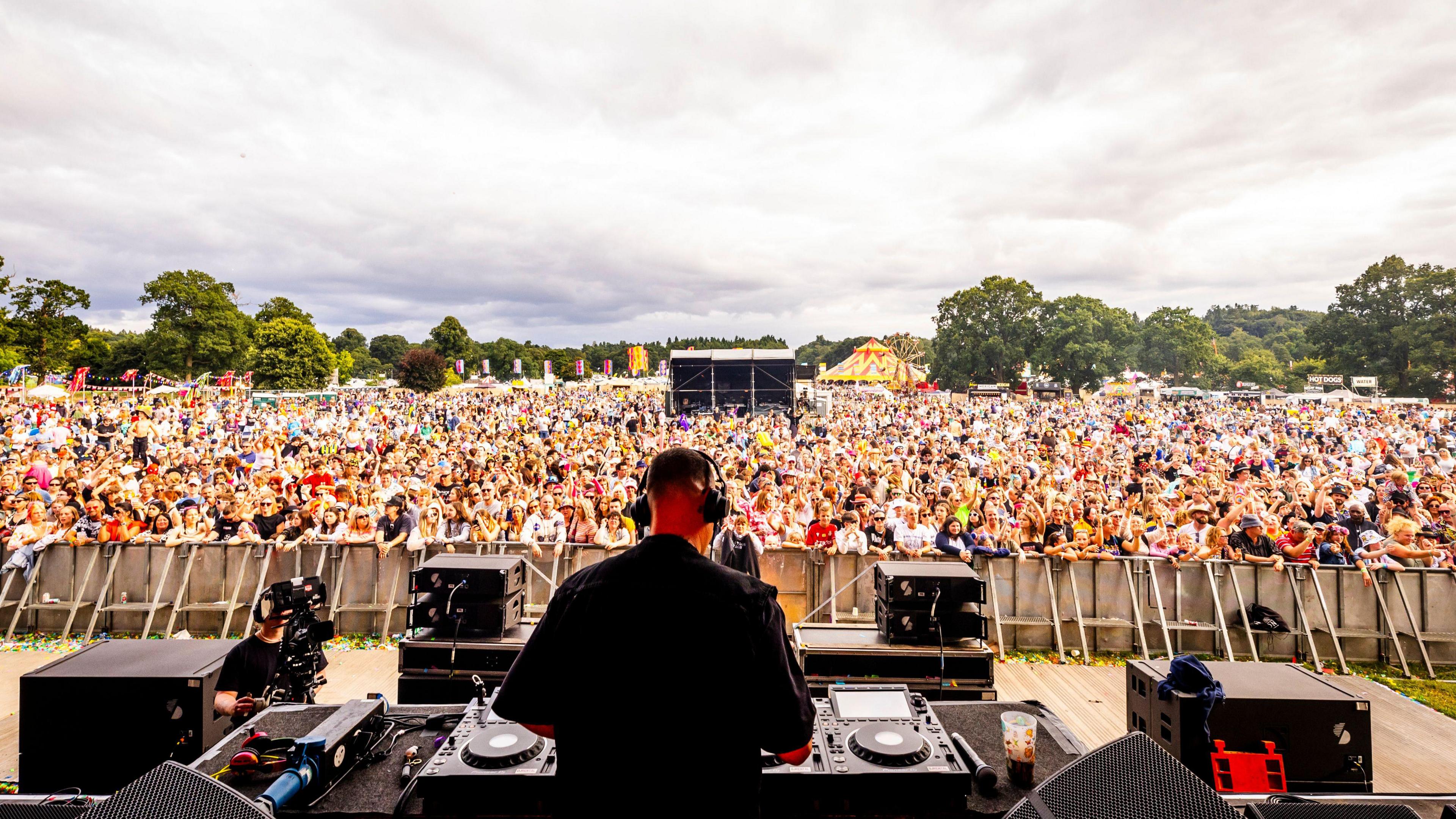 The back of Gok Wan as he performs a DJ set on stage in front of a crowd at Camp Bestival