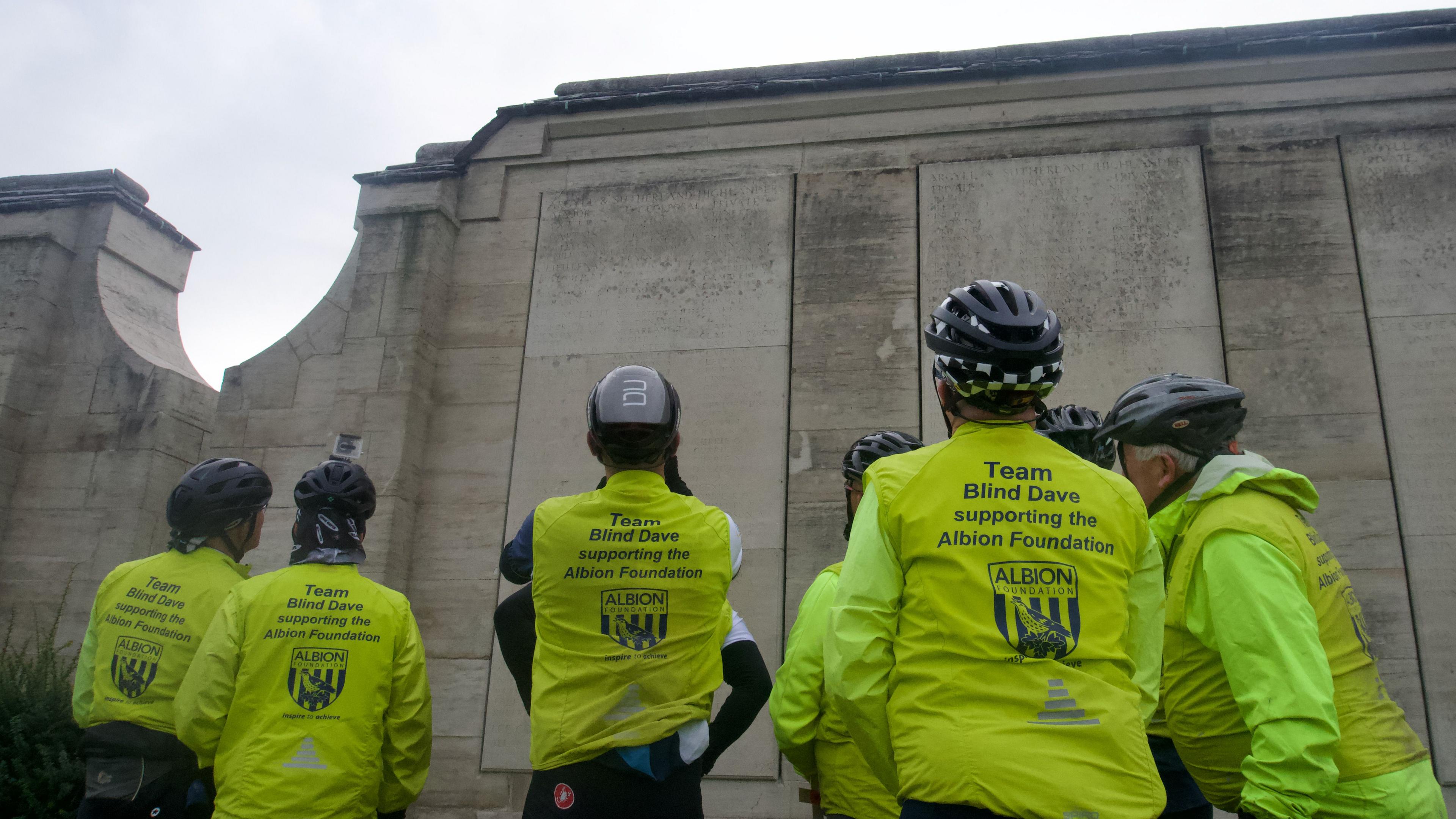 Cyclists look at a list on names on a war memorial