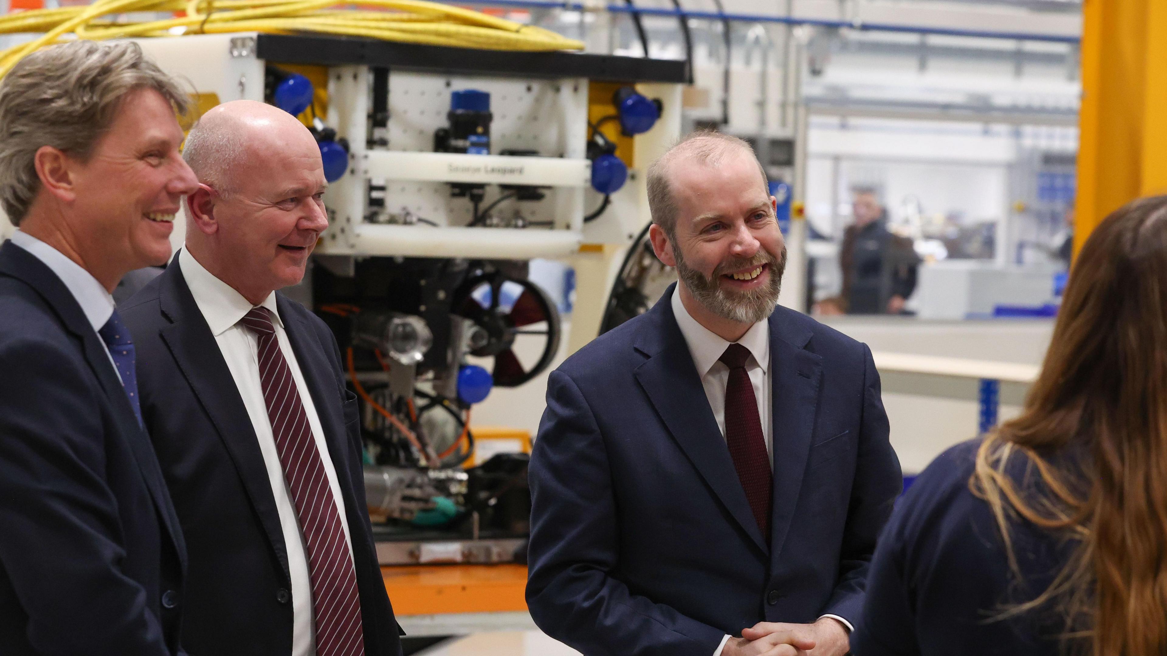 Jonathan Reynolds smiling and talking to a woman, whose face cannot be seen, stood next to Mr Johansson in what appears to be Saab's factory.