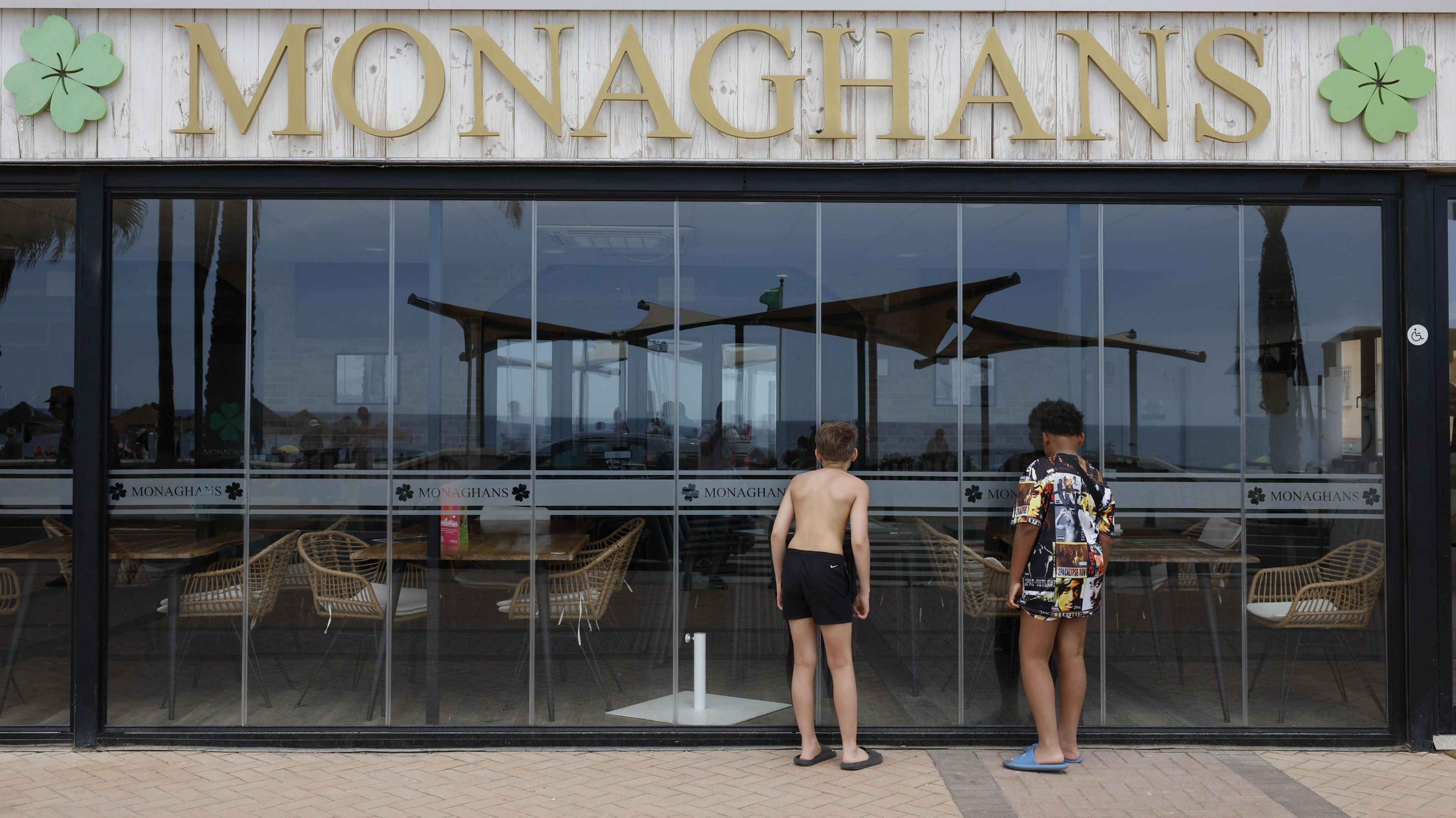 Two children, with their backs to the camera, look in the glass shuttered doors which seal off the outdoor seating area of Monagahans bar.