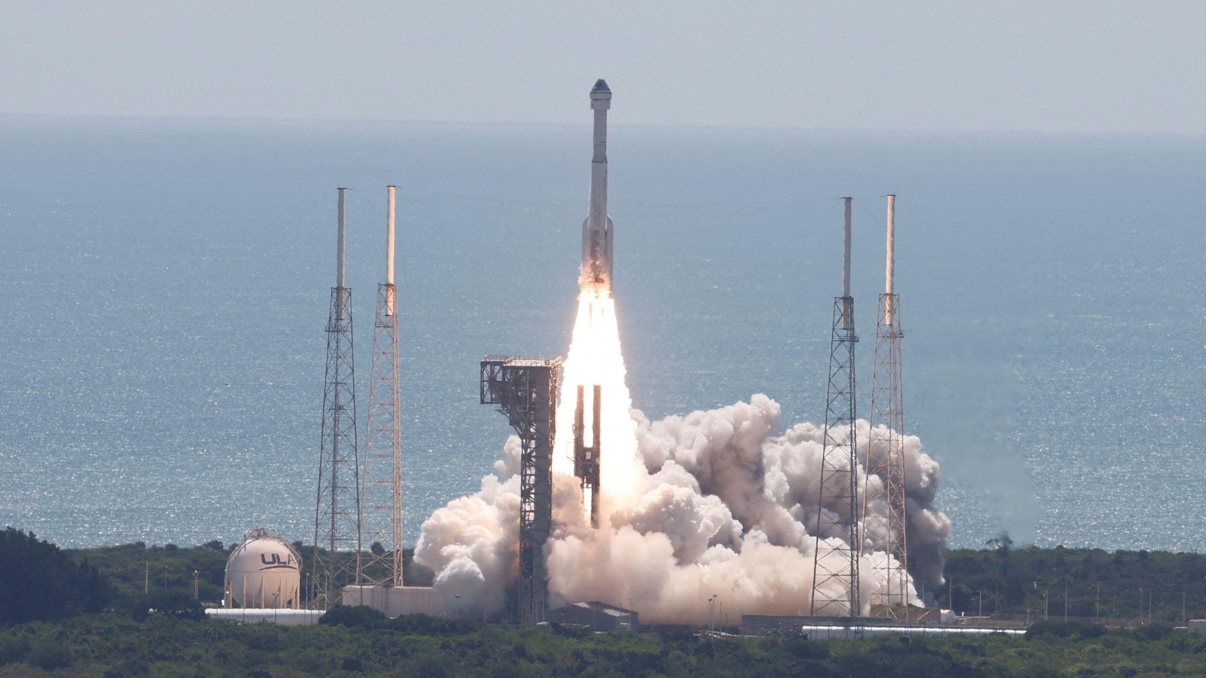 A far away photo of a space rocket launching, with a plume of smoke and cloud caused by the engines