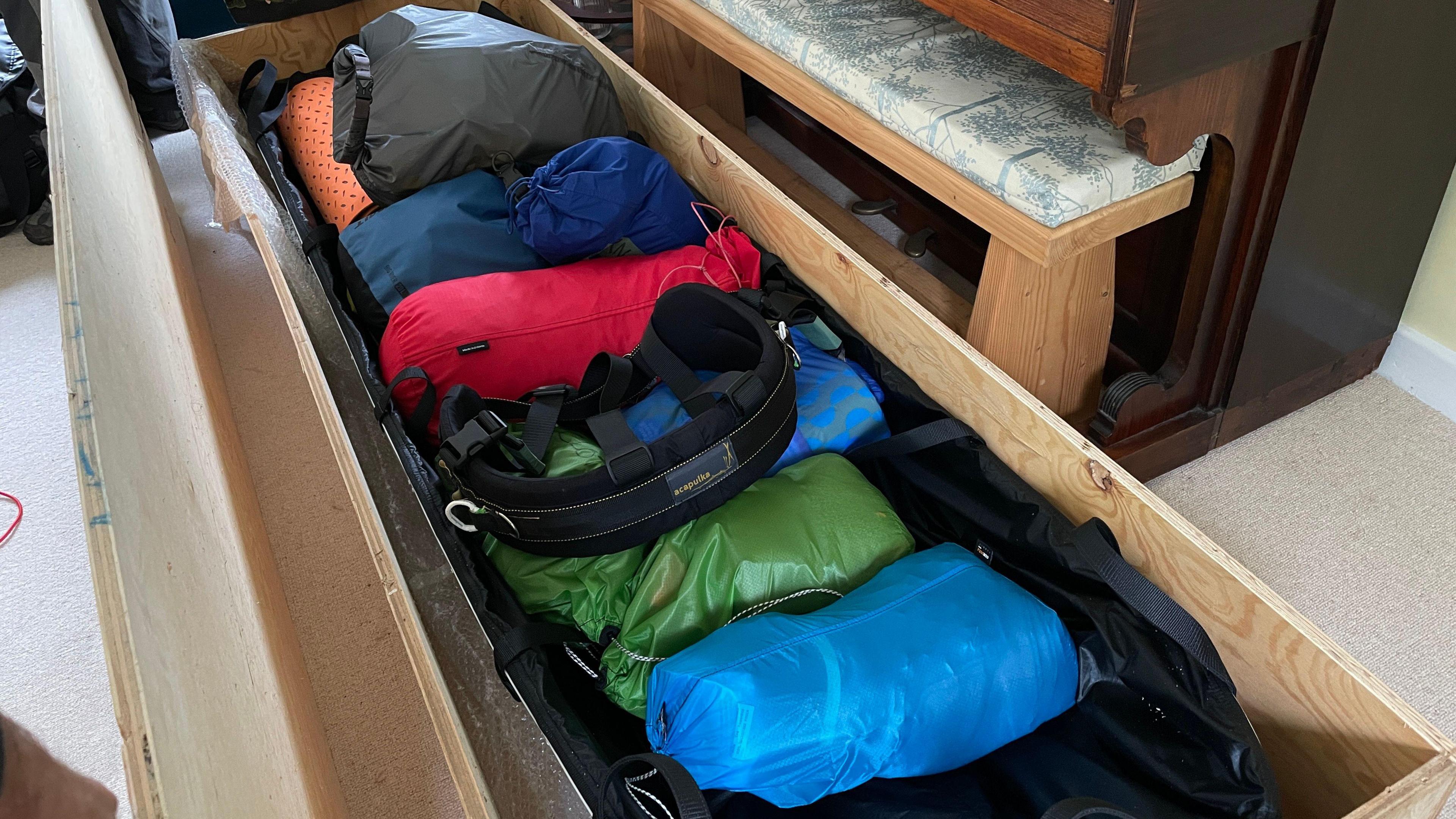 The picture is of Jonny's equipment within a wooden box. There is a blue, green, red and orange bag within the picture laid horizontally next to one another.