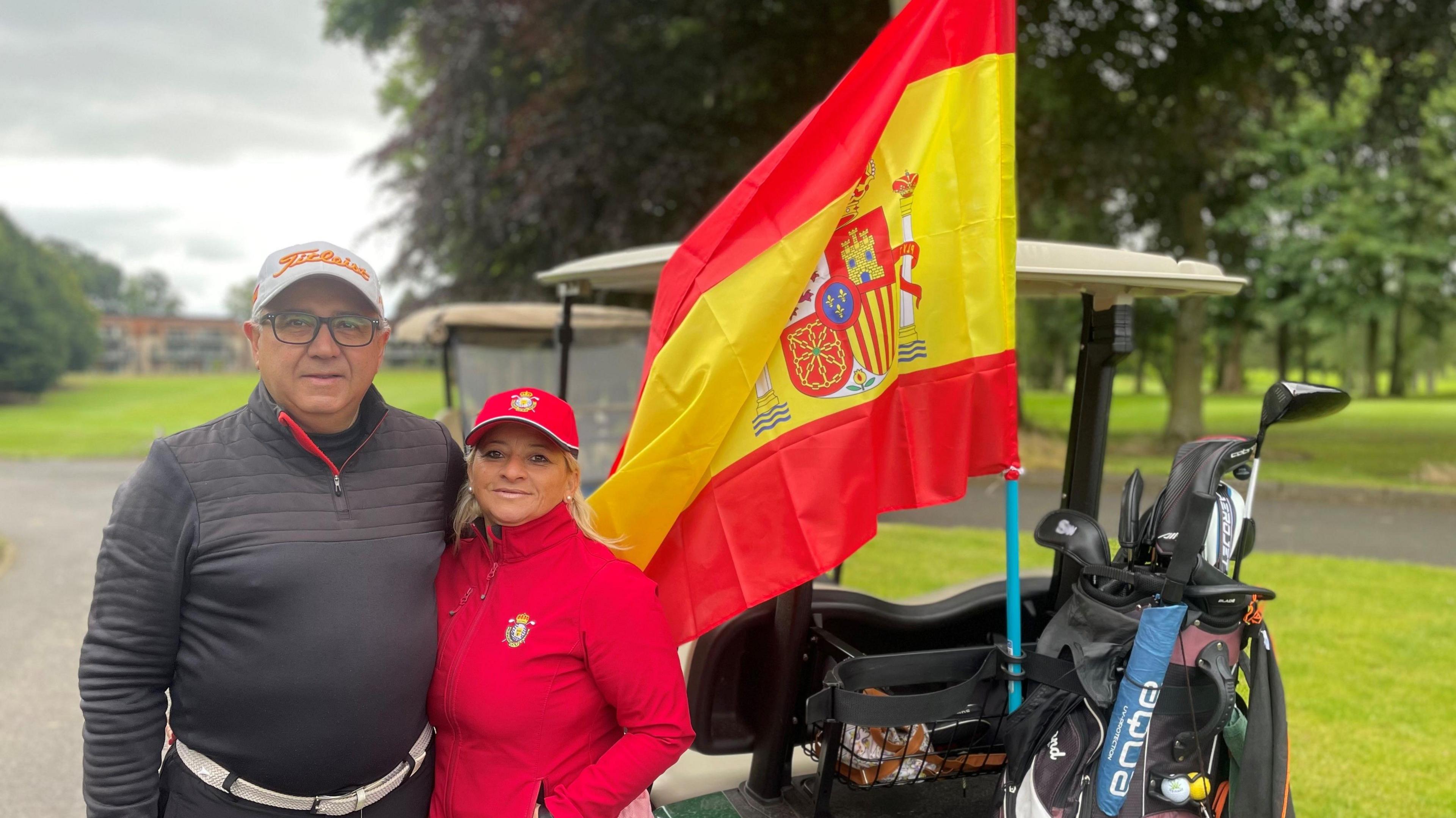 A man and a women stand beside a golf buggy 