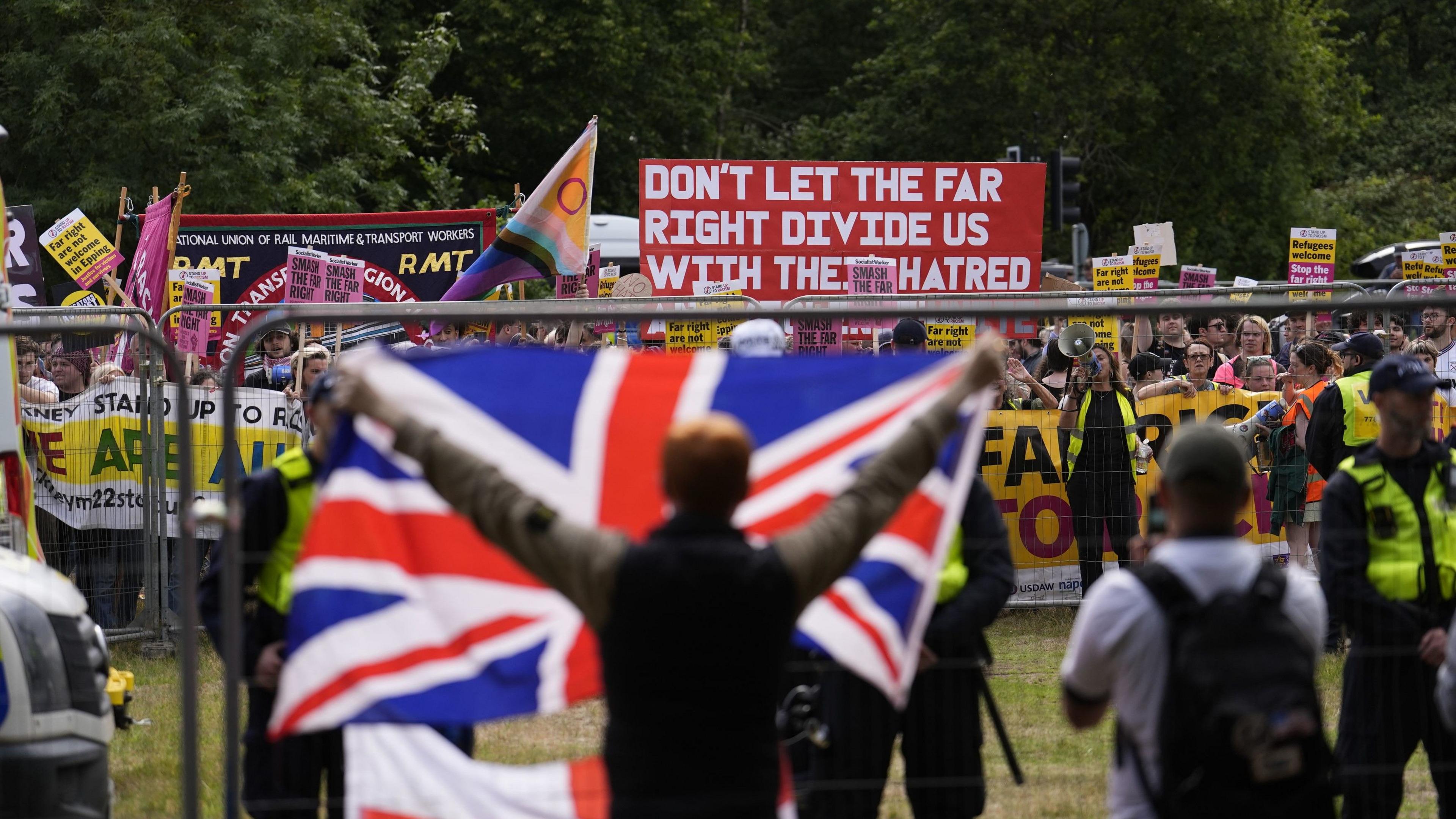 A man holds a union jack flag up to rival protesters who have flags and banners, one of which reads: "Don't let the far right divide us with their hatred."