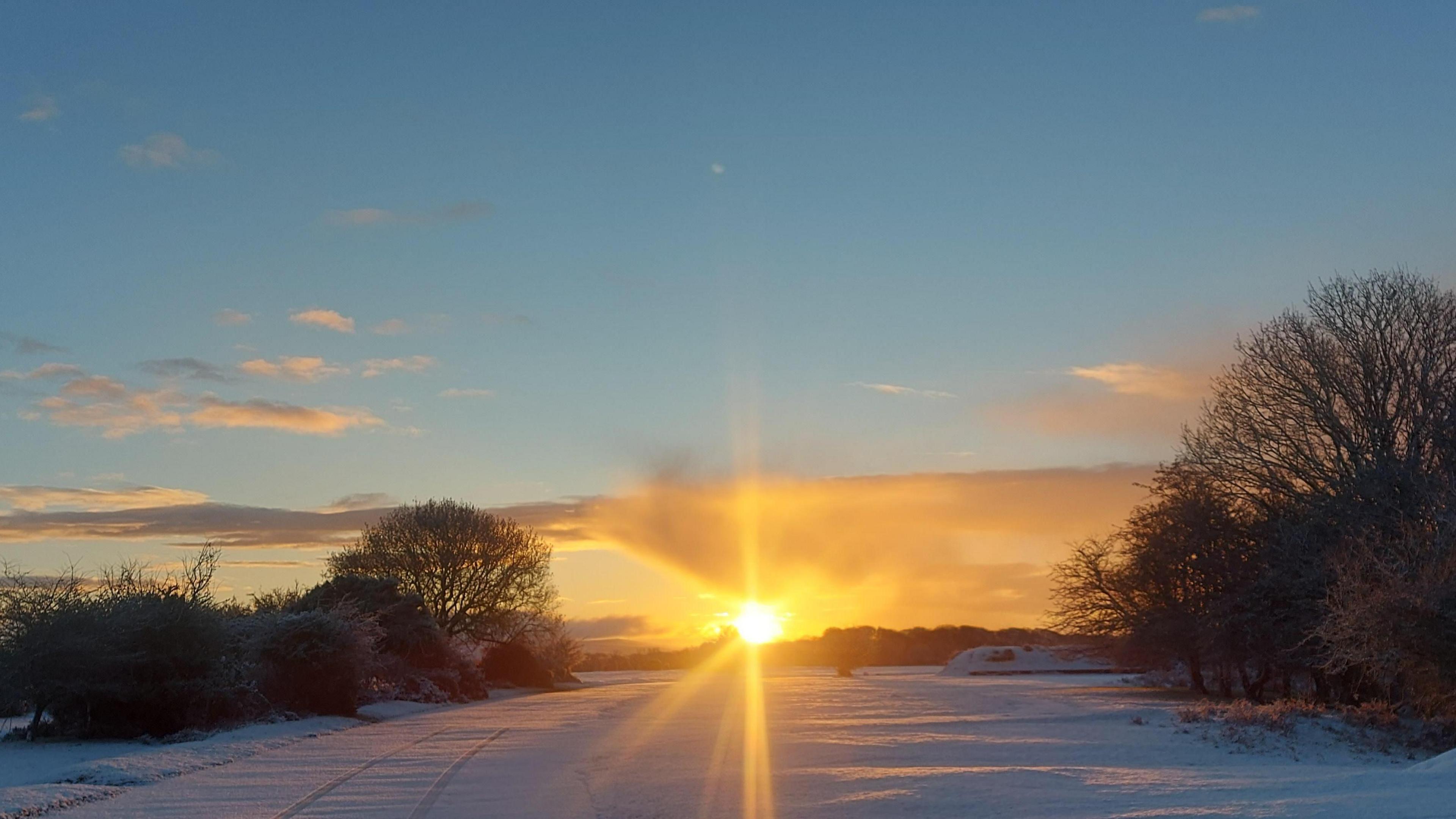 Sunrise over a snow covered area in Plymouth. The sun is shining over the snow. 