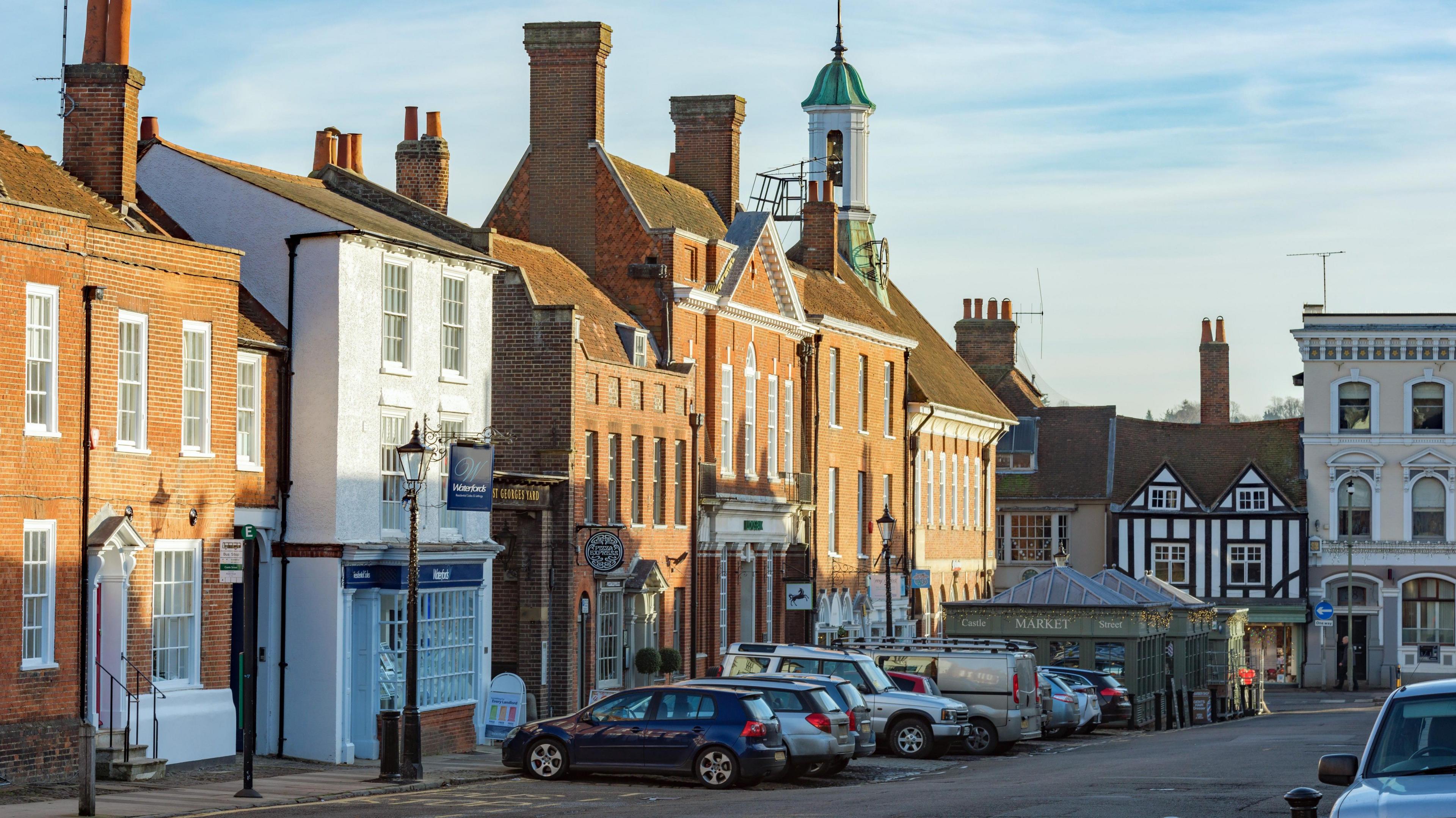 Castle Street in the centre of Farnham is an old street with a mixture of commercial and residential buildings. Cars are parked up in marked bays on the street. Shops comprise estate agencies, restaurants and specialist retail outlets.