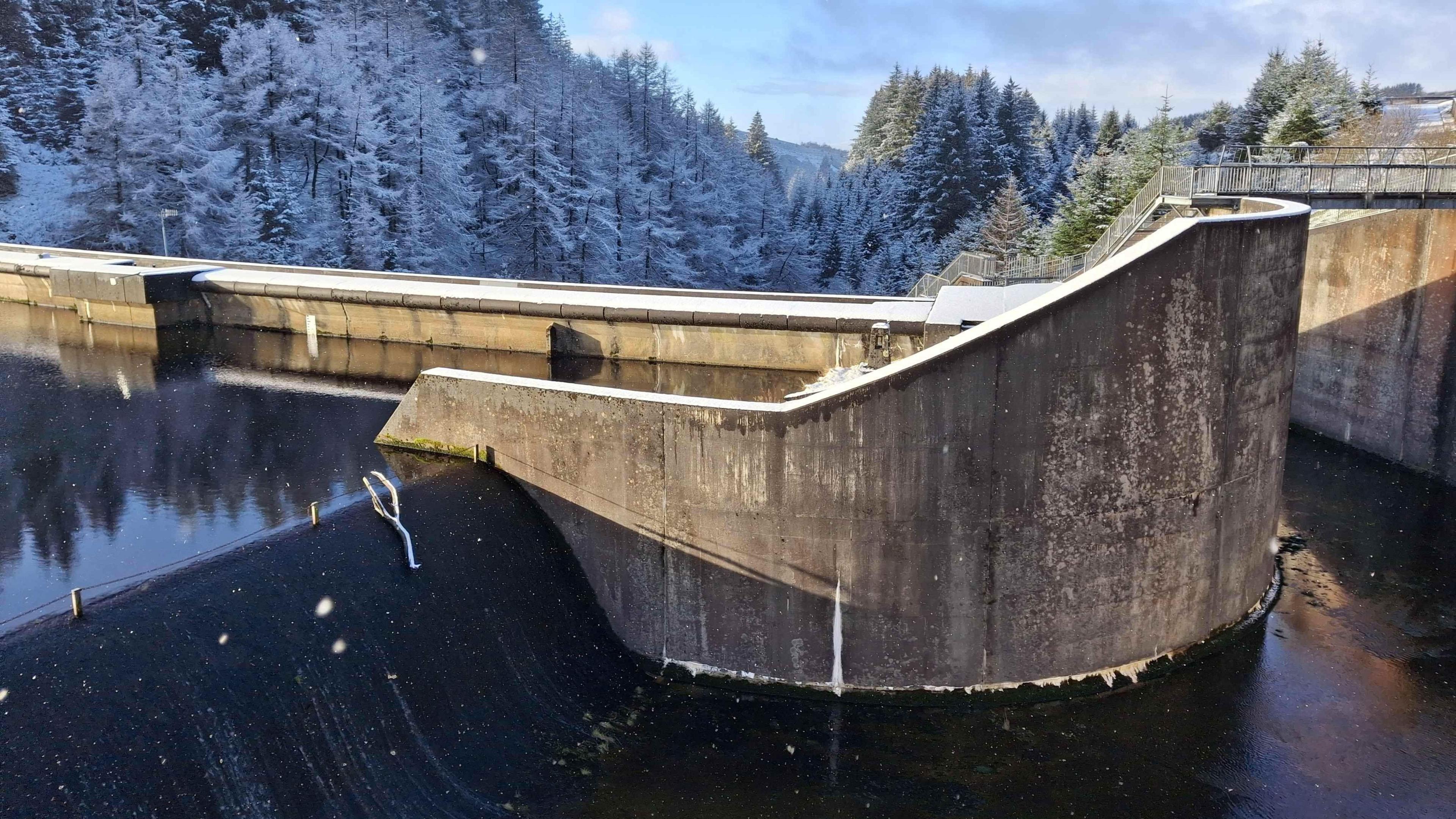 A reservoir with water that looks frozen. Snow covered trees care in the background.