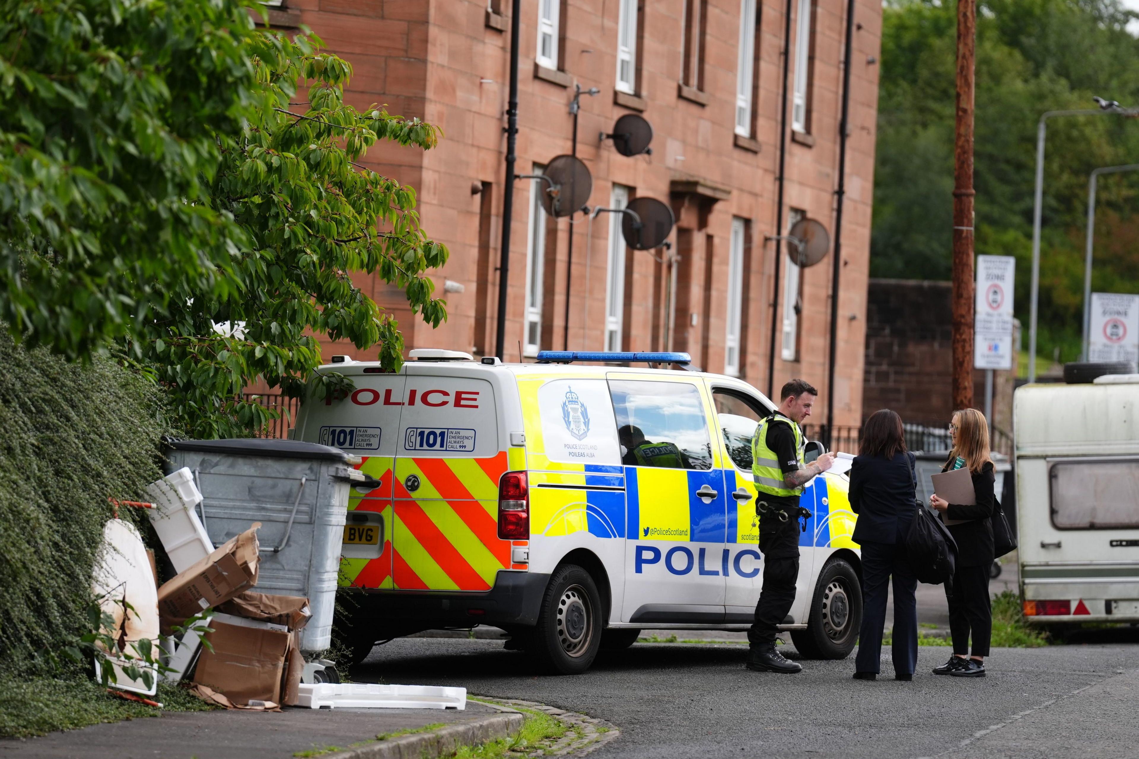 Exterior of a block of red brick flats with a police van outside and a group of officers