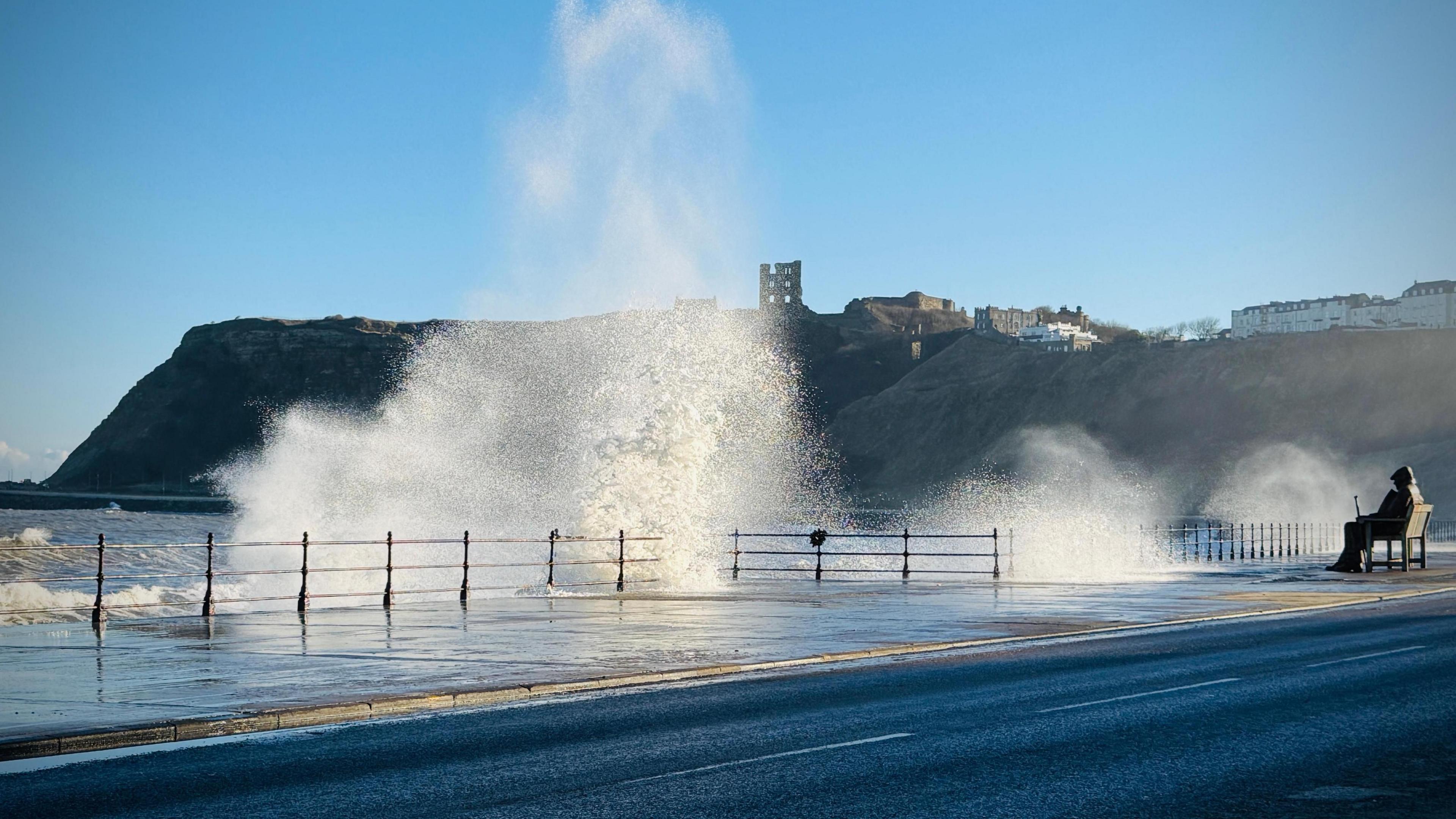 Waves crash against the seafront in Scarborough. the town's castle is visible on the cliffs behind.