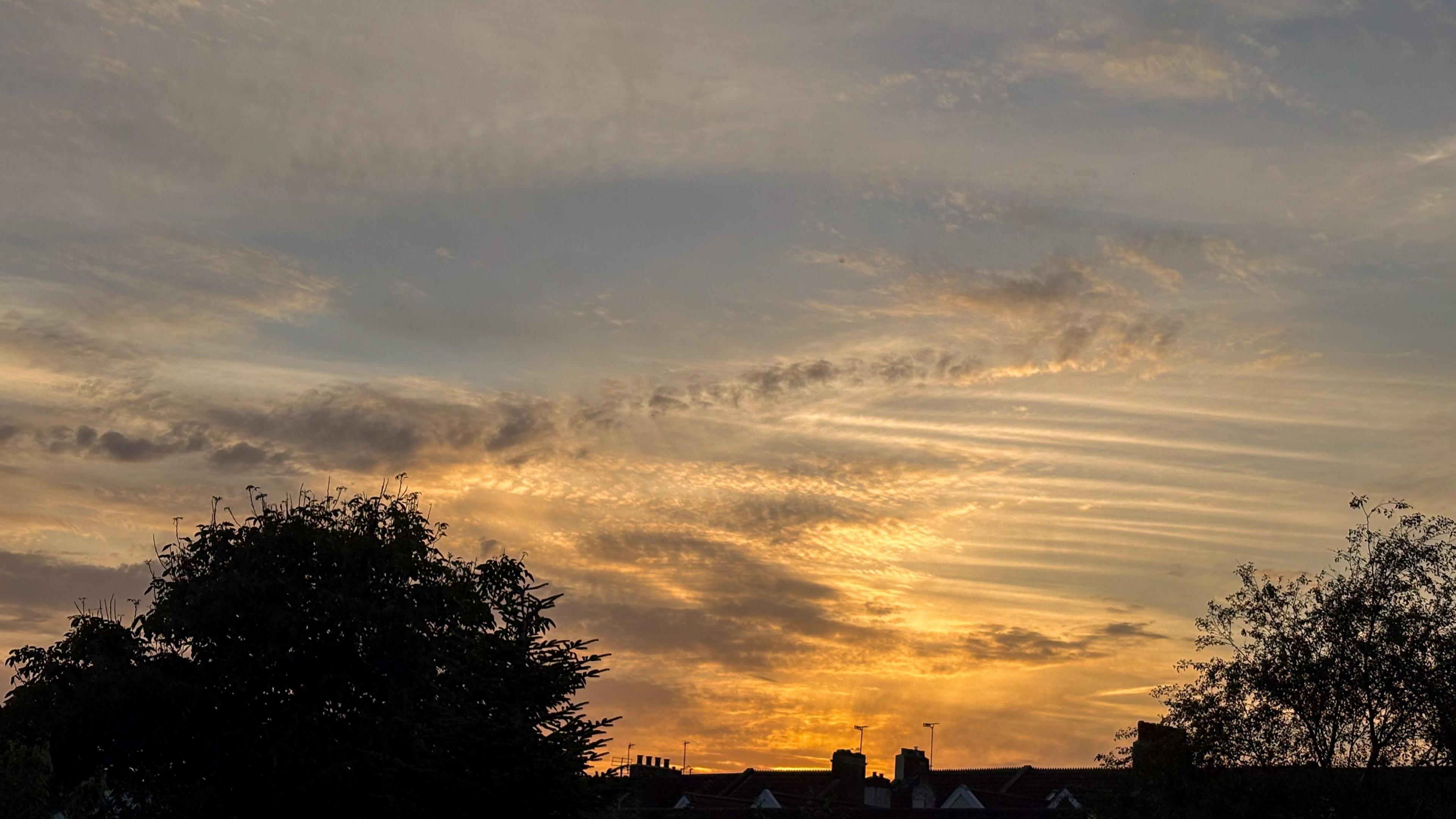A light orange sunset over the roofs of a terrace of houses. 