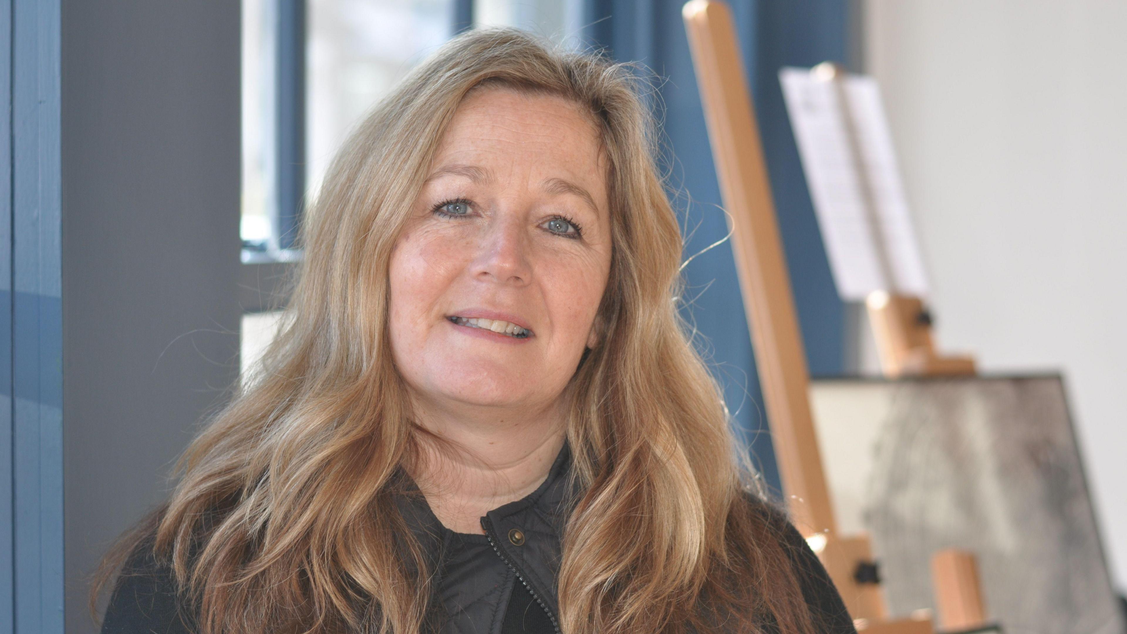 Anneley Pickles, who has long blonde hair, smiles at the camera as she is photographed in an art shop.