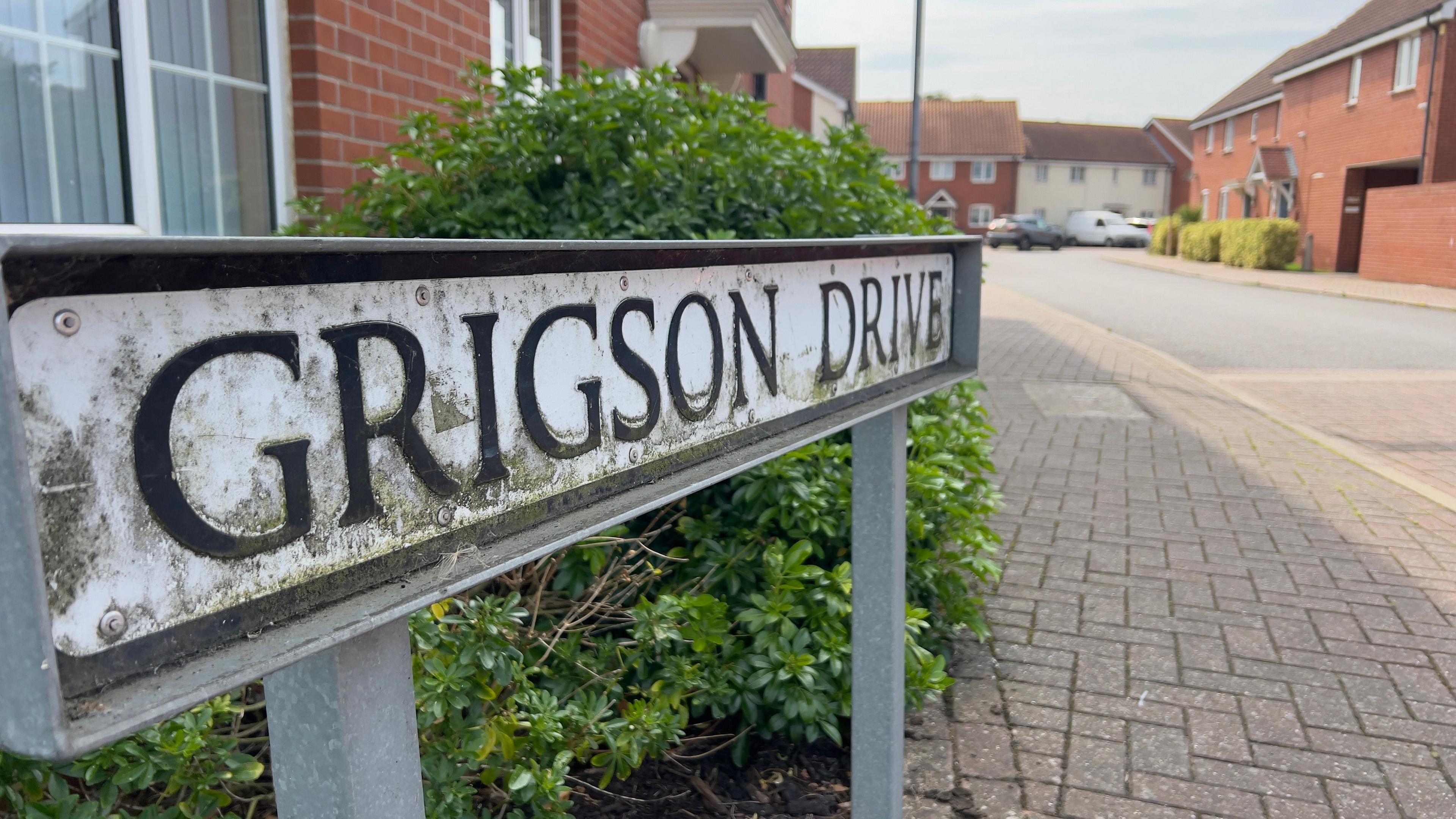 A road sign reading "Grigson Drive" with residential houses in the background. 