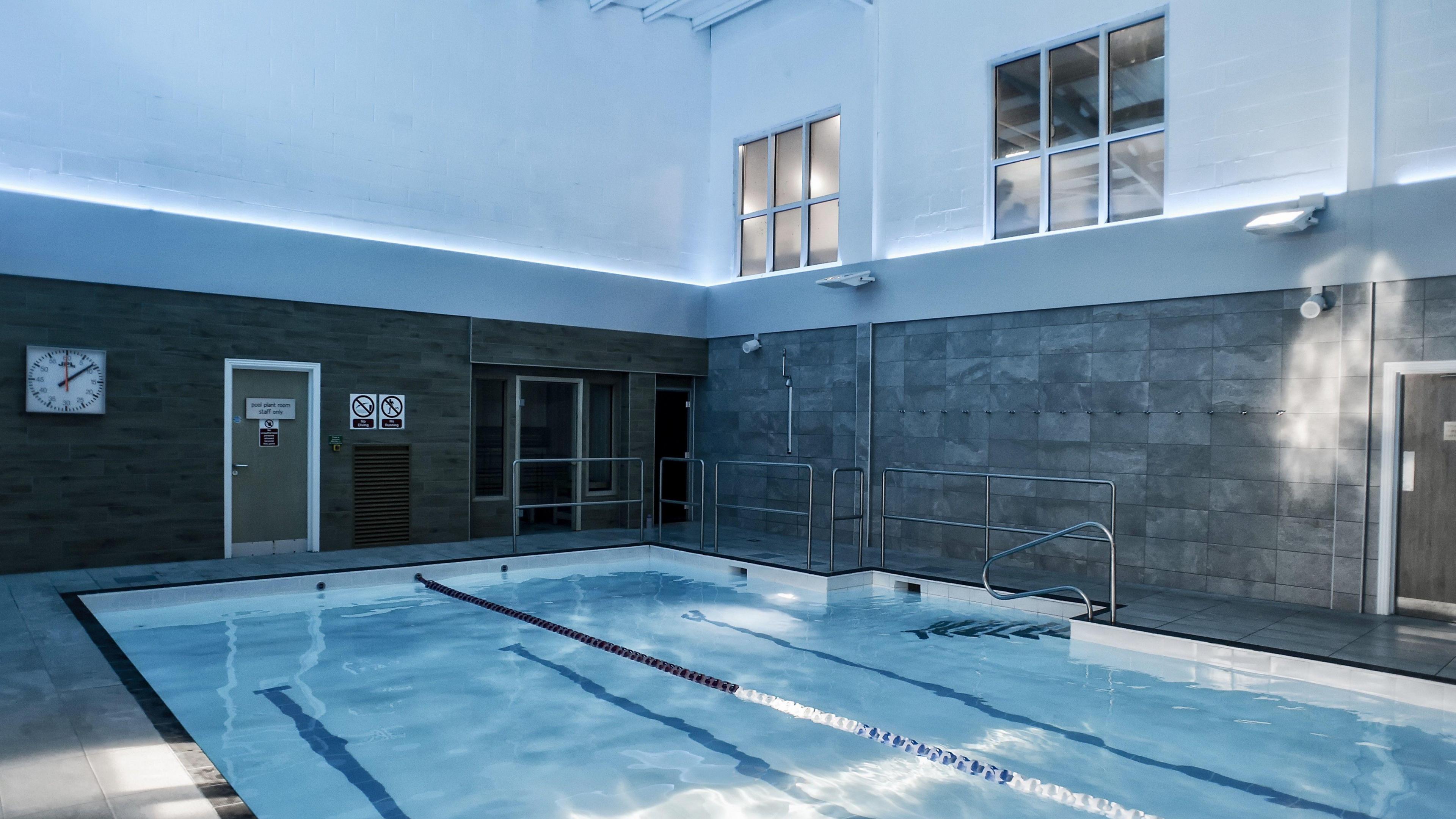 An indoor swimming pool. It has blue tiles and blue and white lane dividers. The walls are tiled grey.