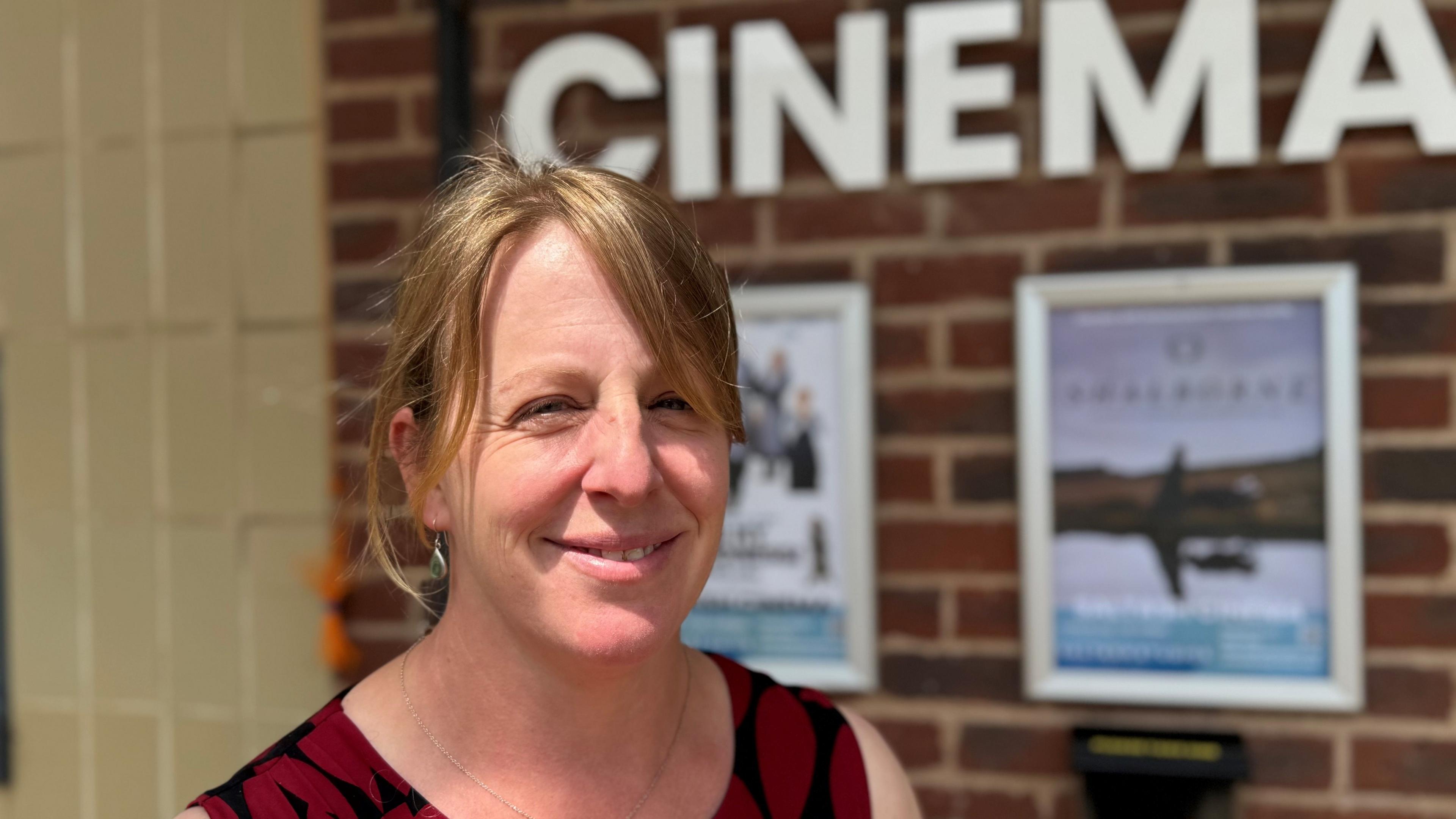 Woman with blonde hair and smiling to the camera standing in front of the new cinema building
