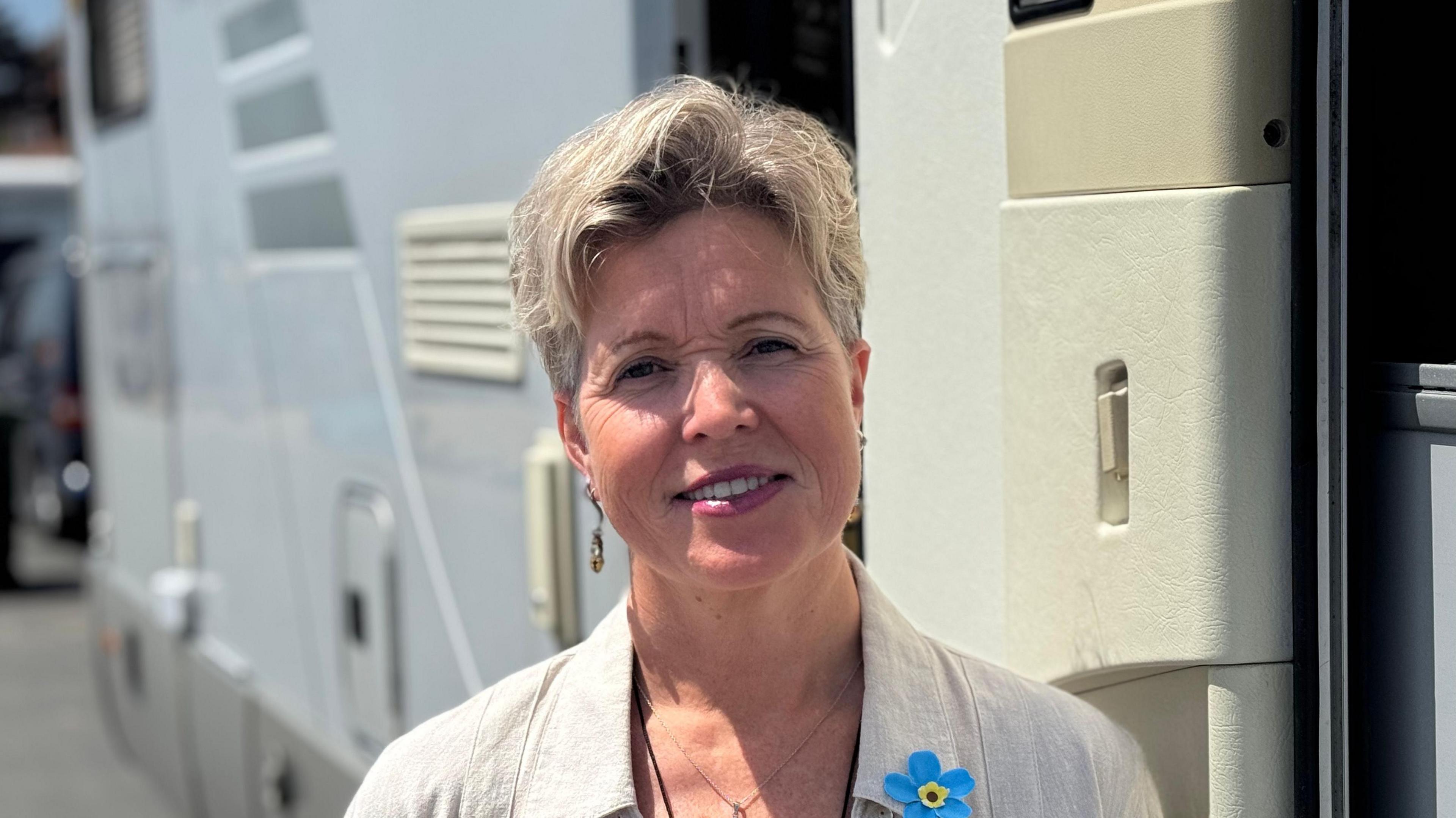A head and shoulders shot of Katrina Cable. She is smiling and looking directly into the camera. She is wearing a cream shirt with a lace top beneath it. She is standing in front of her motorhome.