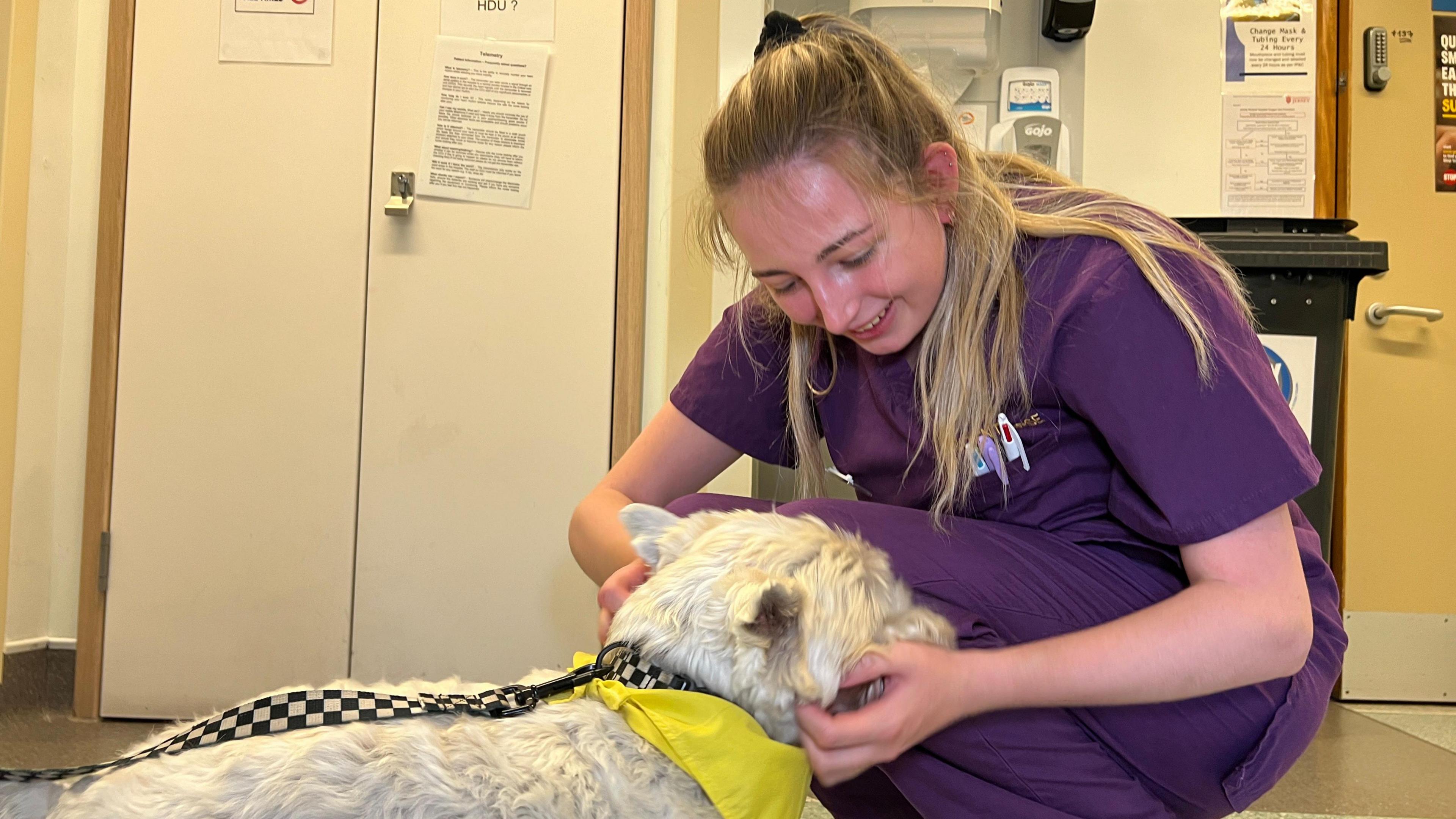 A member of staff on the ward kneels to gently tickle Frankies face