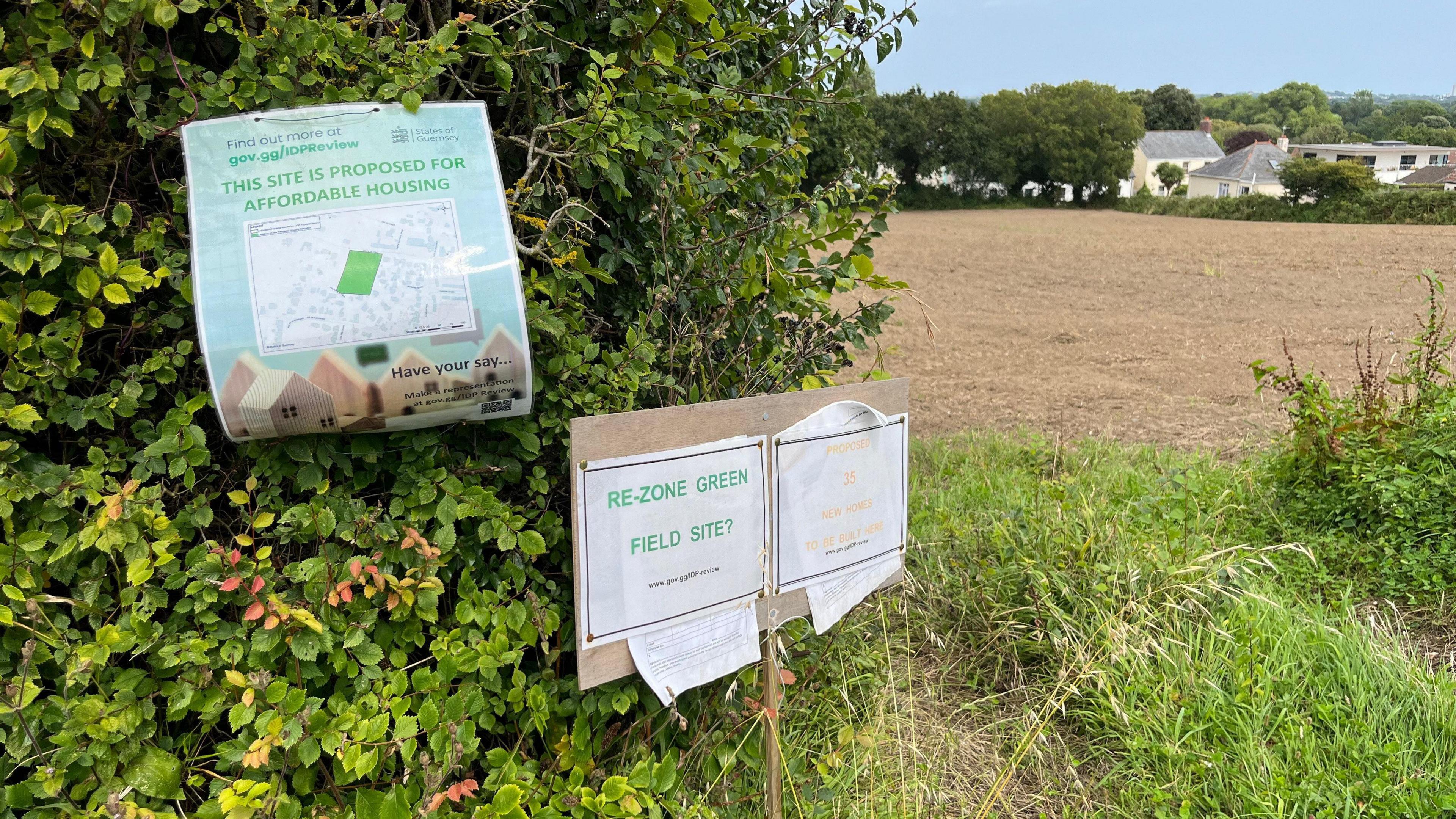 Three signs by a hedge in front of a freshly-ploughed field