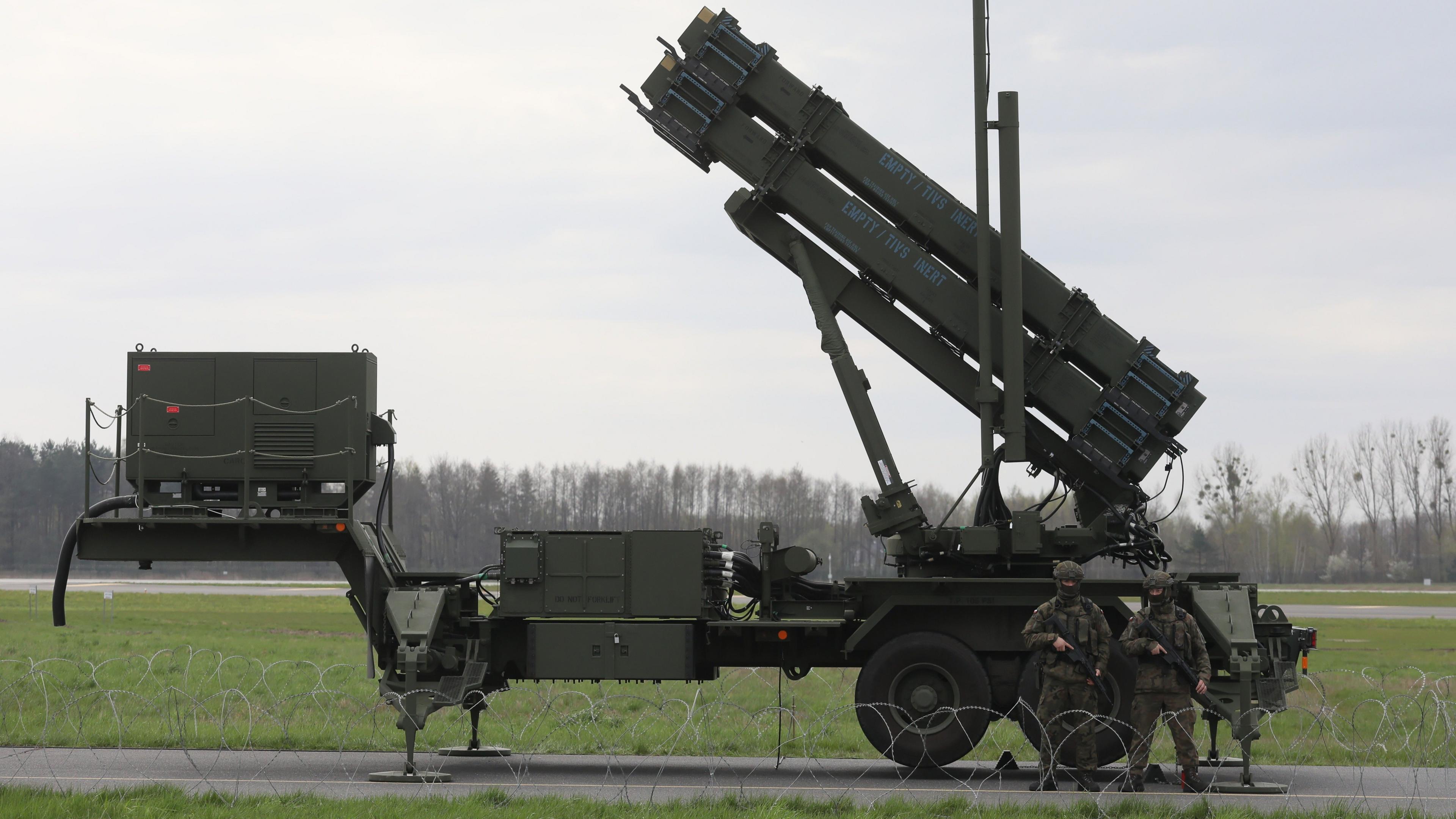 Two armed people in camouflage stand in front of a Patriot missile system