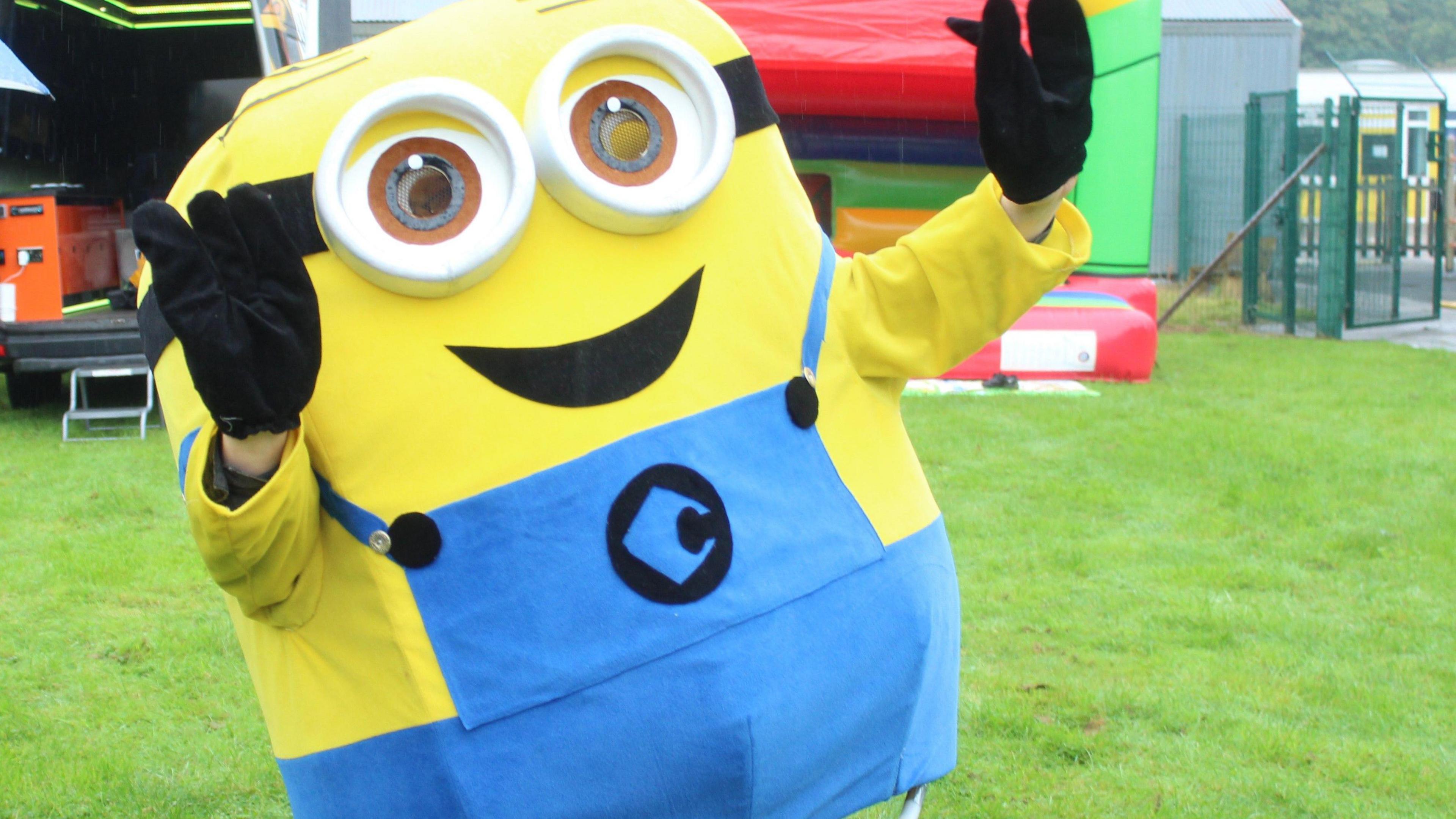 A life-size yellow and blue Minion character, as depicted in the Despicable Me film franchise, smiles and holds up its hands