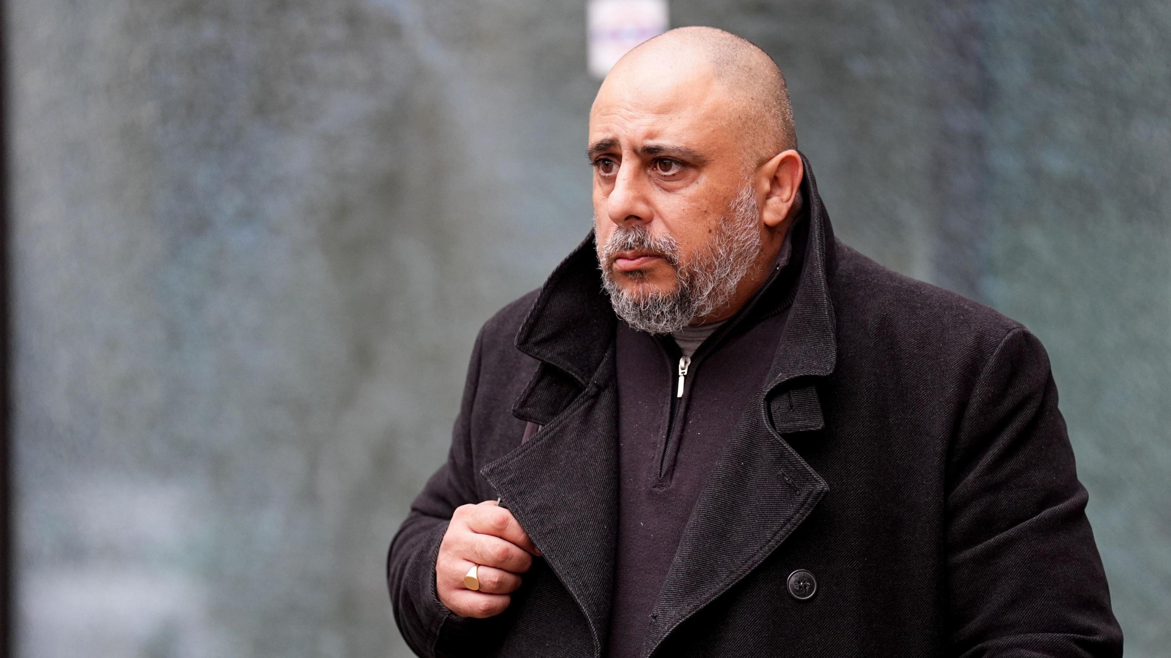 Ozgay Chevat, a bald headed man with a beard, wearing a dark coloured top with a zip under a dark colour corduroy coat, leaving the court.