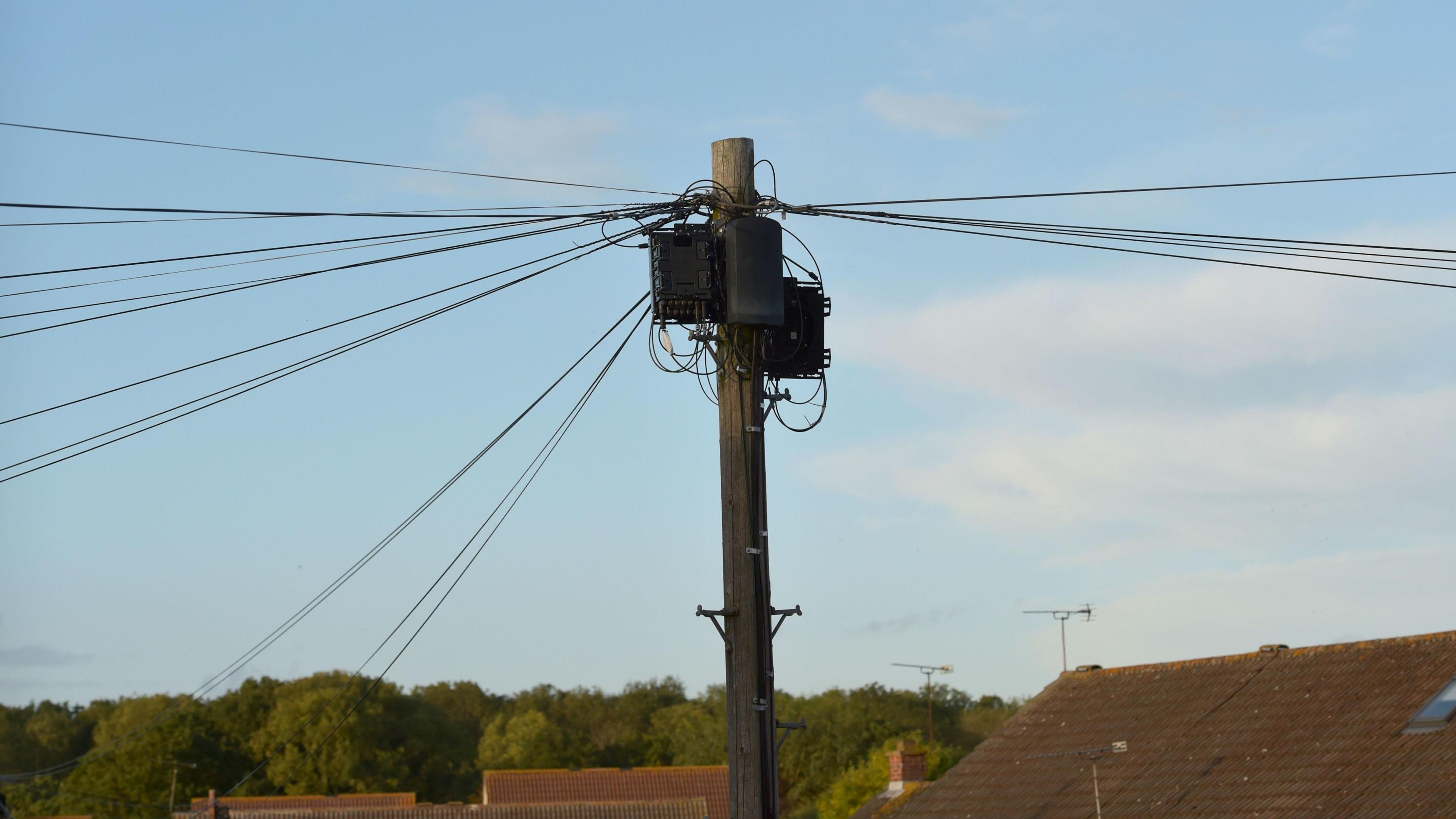 A telegraph pole with cables attached above the rooftops of houses in the background.