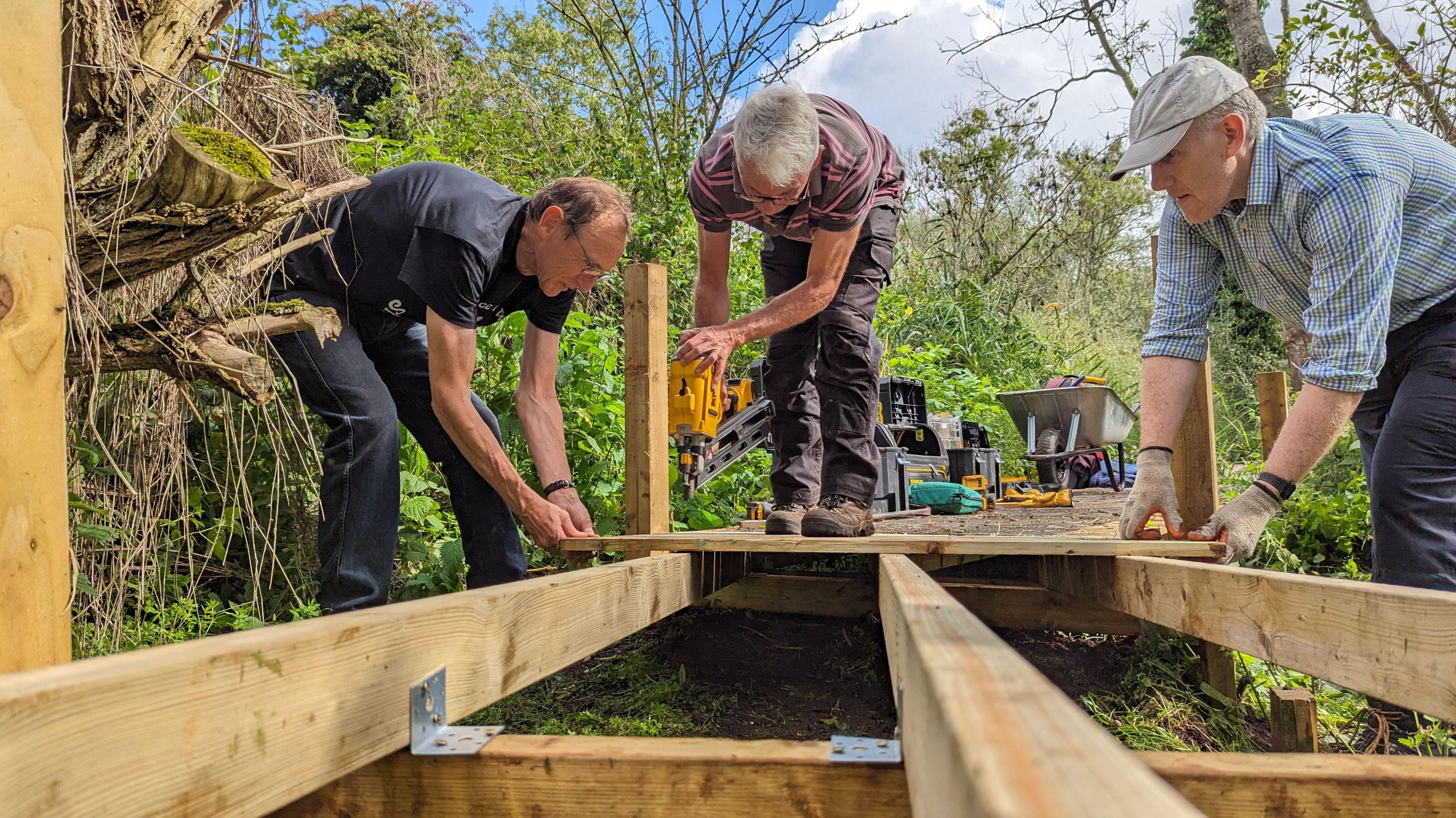 Volunteers working at Hinksey Heights Trail. Three men can be seen fixing planks on the boardwalk. It is a sunny day.