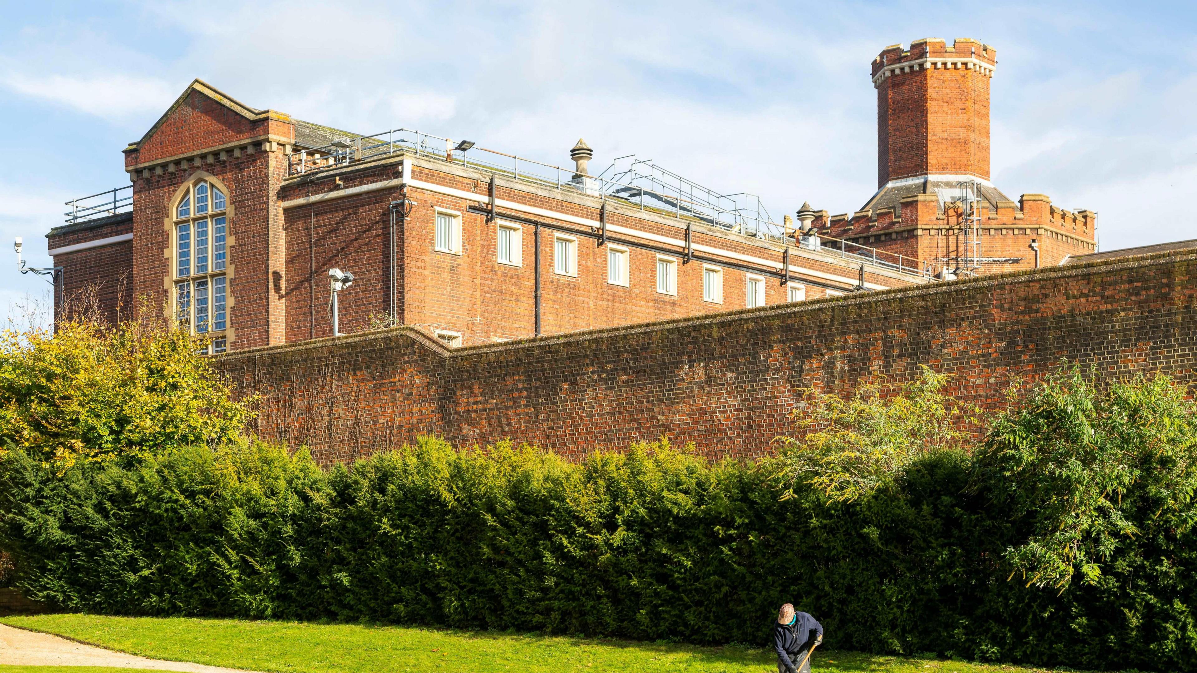 Red brick building, behind a tall red brick wall with green hedges in front of it. This is Reading Jail.