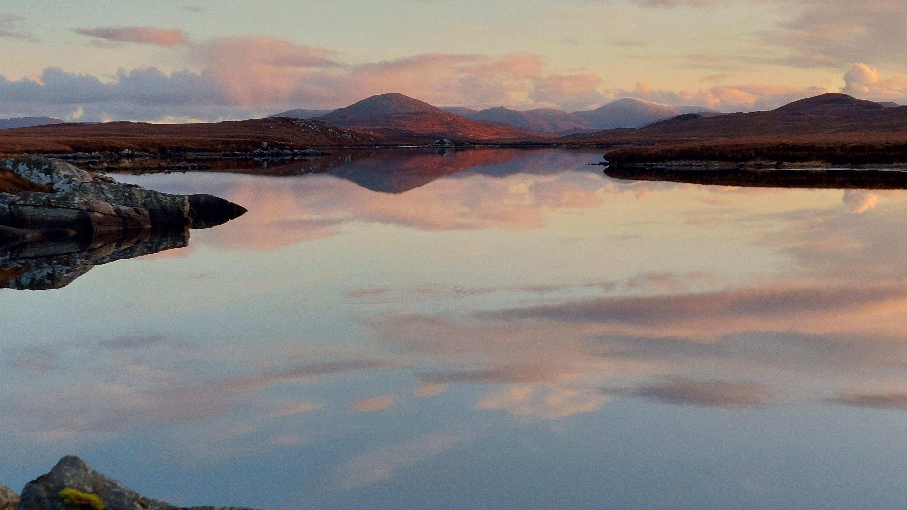 mountains and clouds reflect onto a loch, creating a mirror like effect.