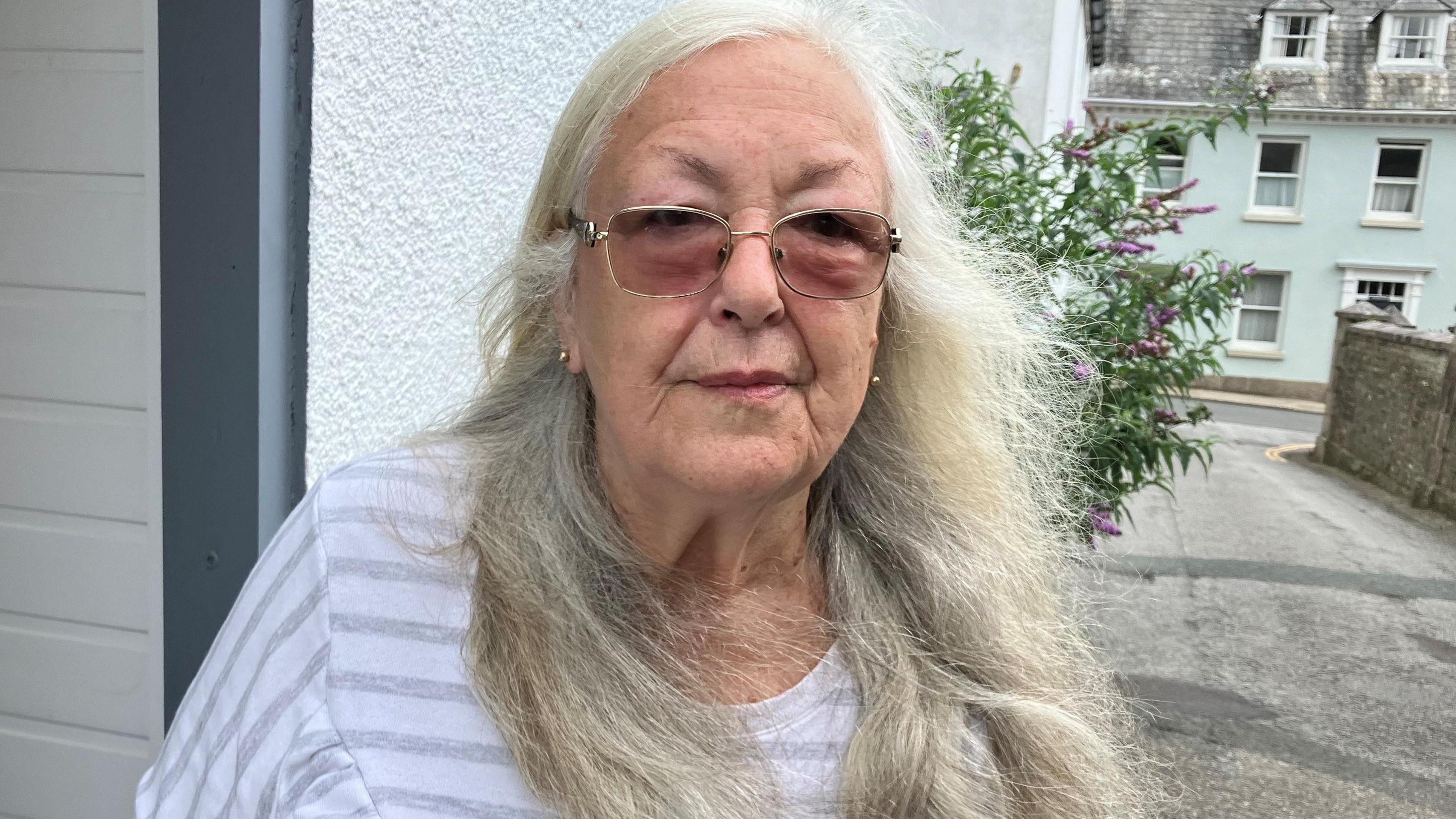 Norma Cattell, with glasses and long grey hair, standing in front of the community larder