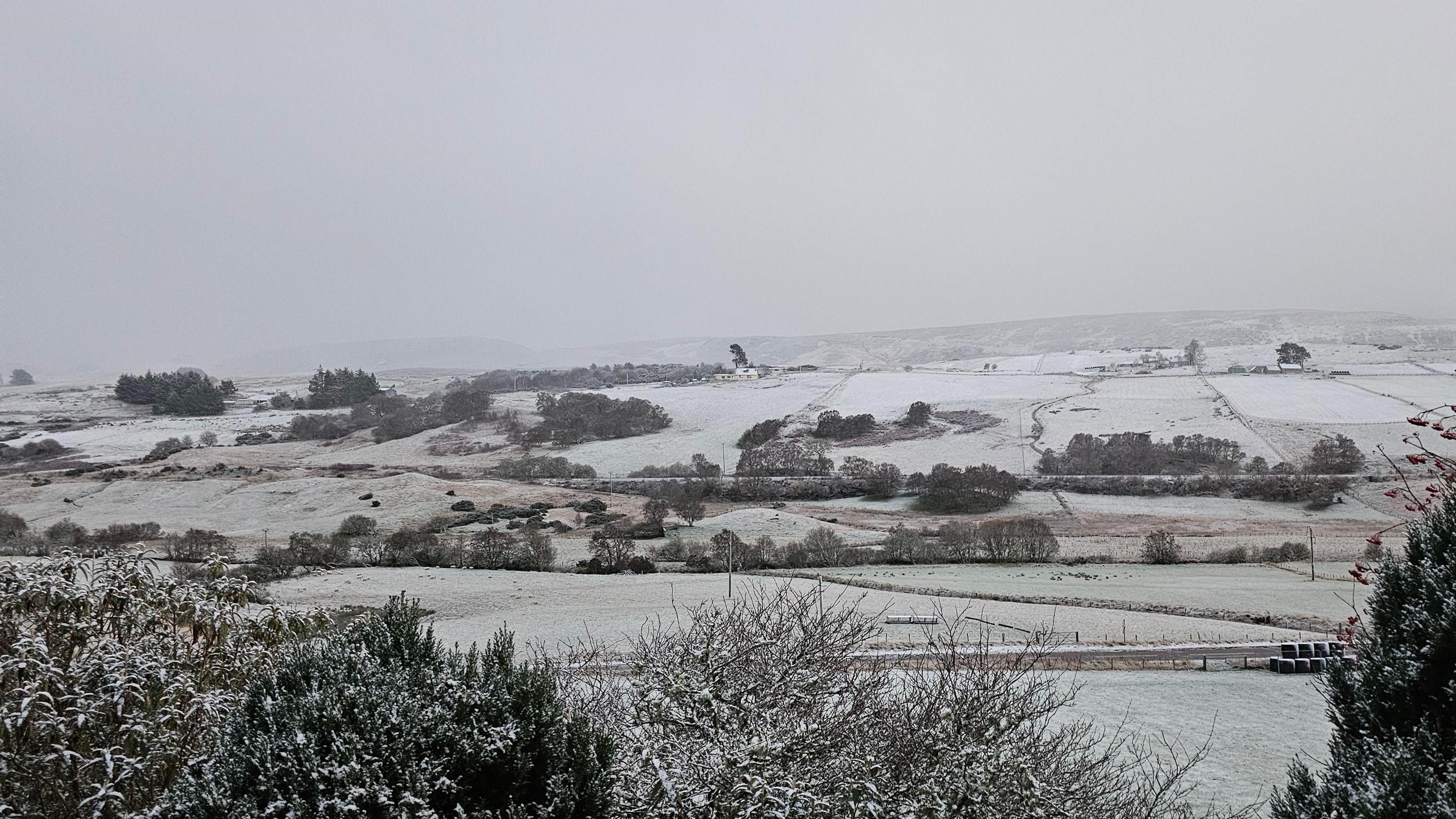 A snow-covered rural of scene of fields and low hills under a grey sky