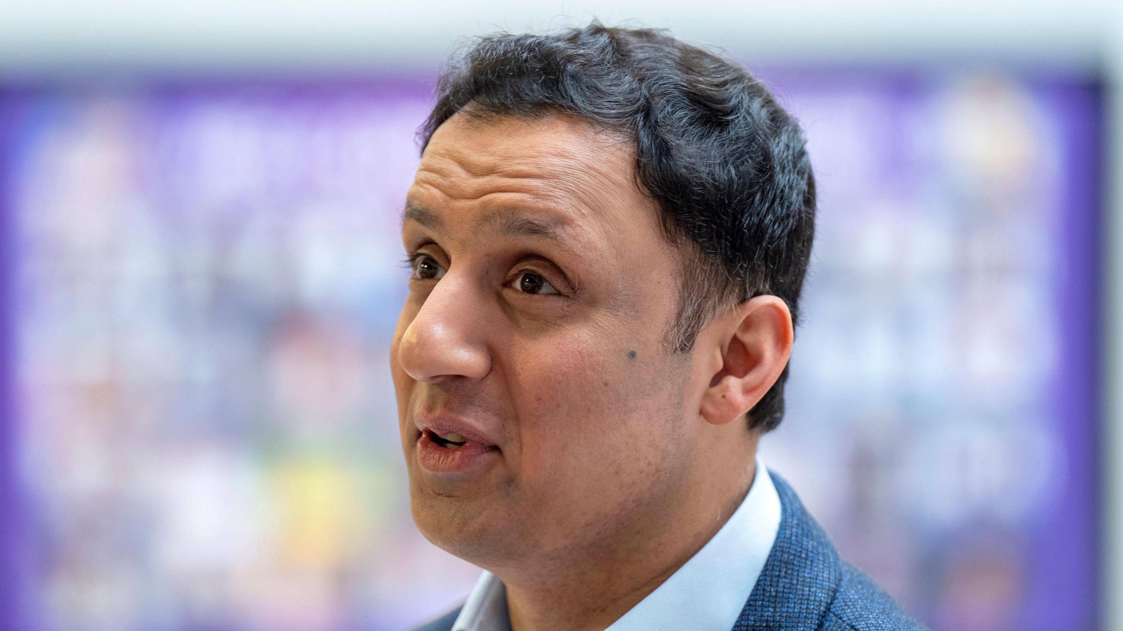Anas Sarwar speaking at an event- he has dark black hair and is wearing a suit.