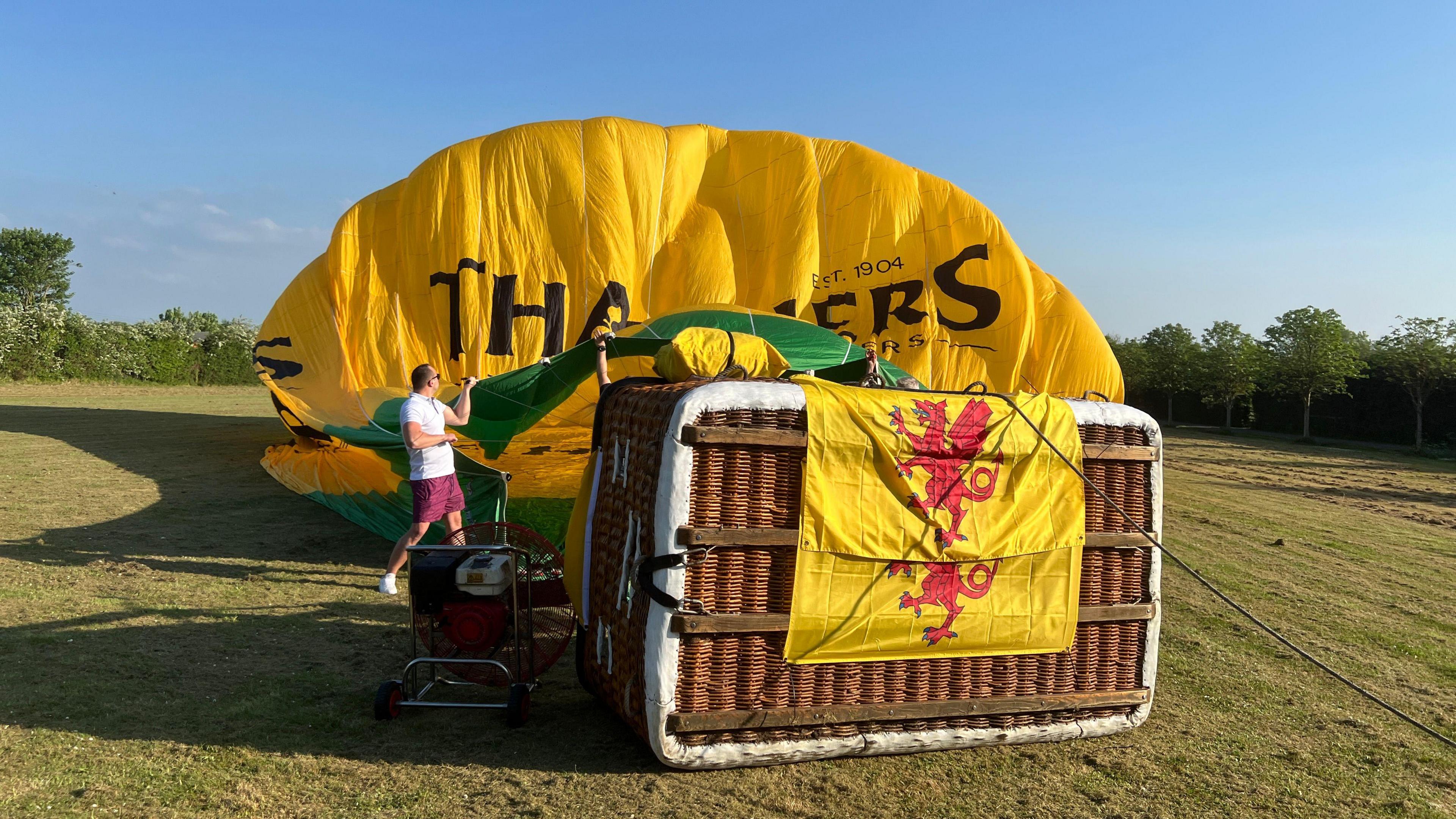 A hot air ballon is on the ground. On the bottom of the basket are two Somerset flags.