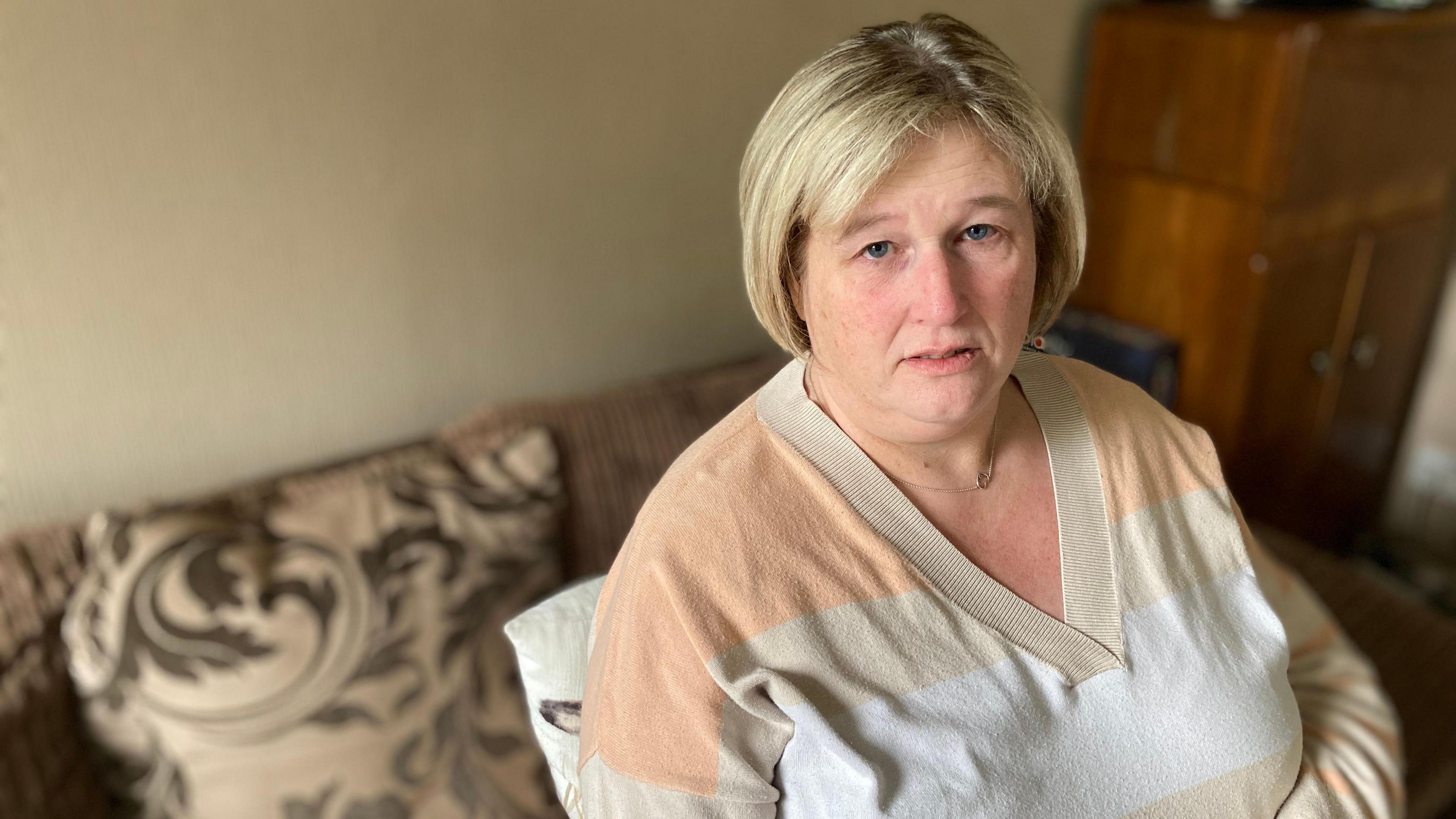 A woman sits on sofa. She is looking into the camera. 