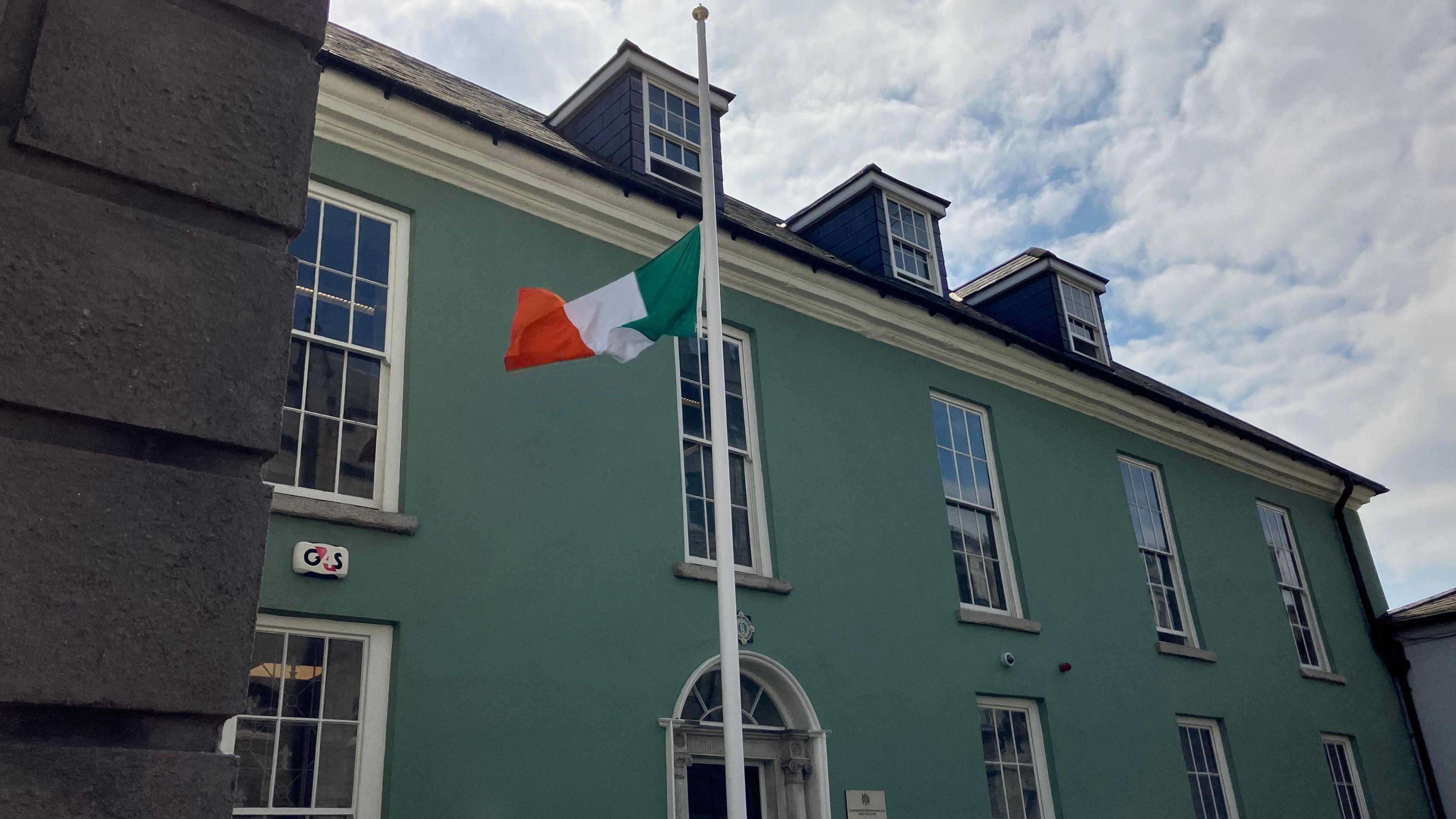 Irish tricolour flying at half-mast on a white pole at Dublin Metropolitan Regional Headquarters at Dublin Castle - the building behind the flag is green