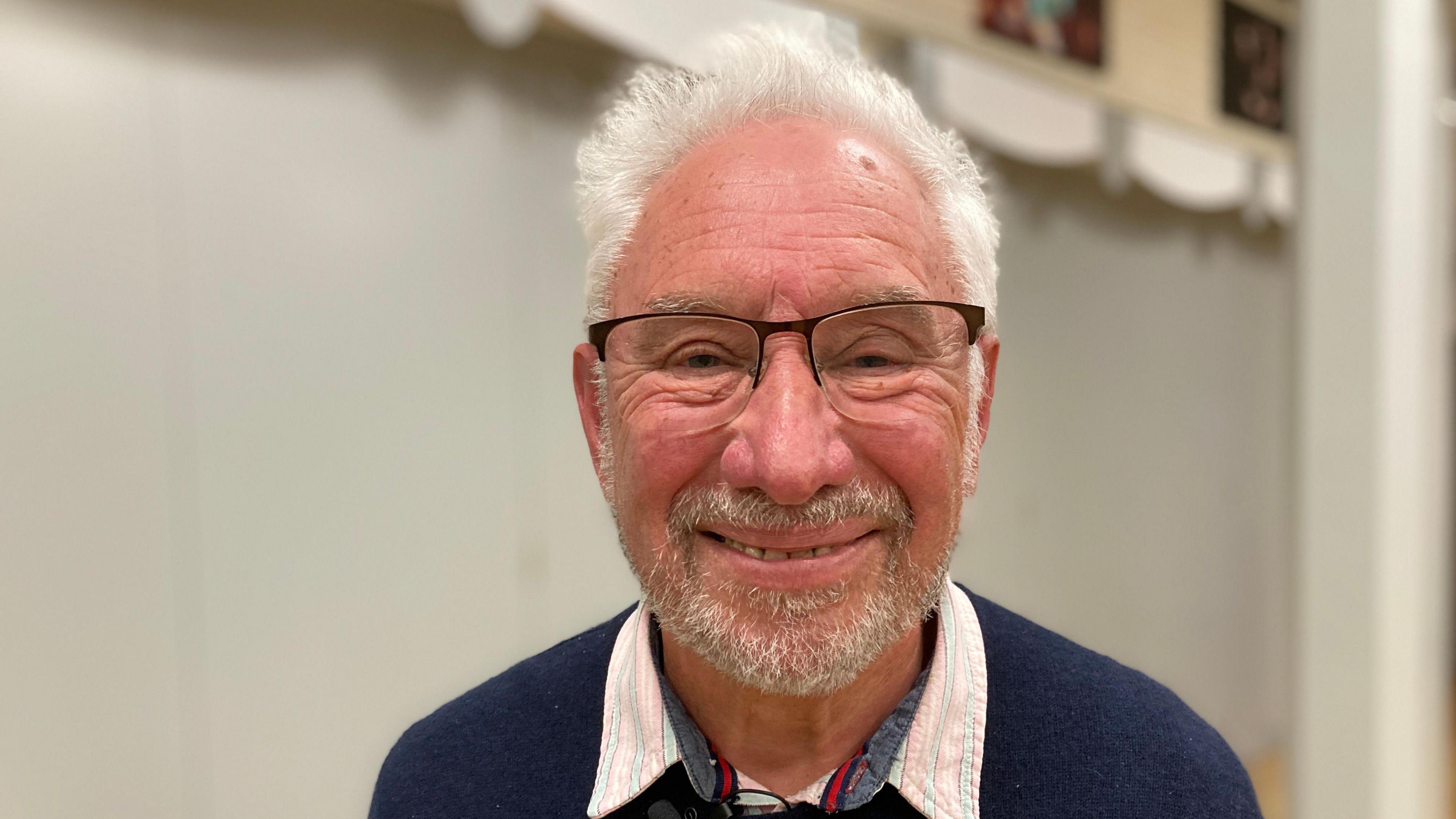 Carl Pearce is looking directly into camera and is smiling. He has white hair, a beard and glasses.