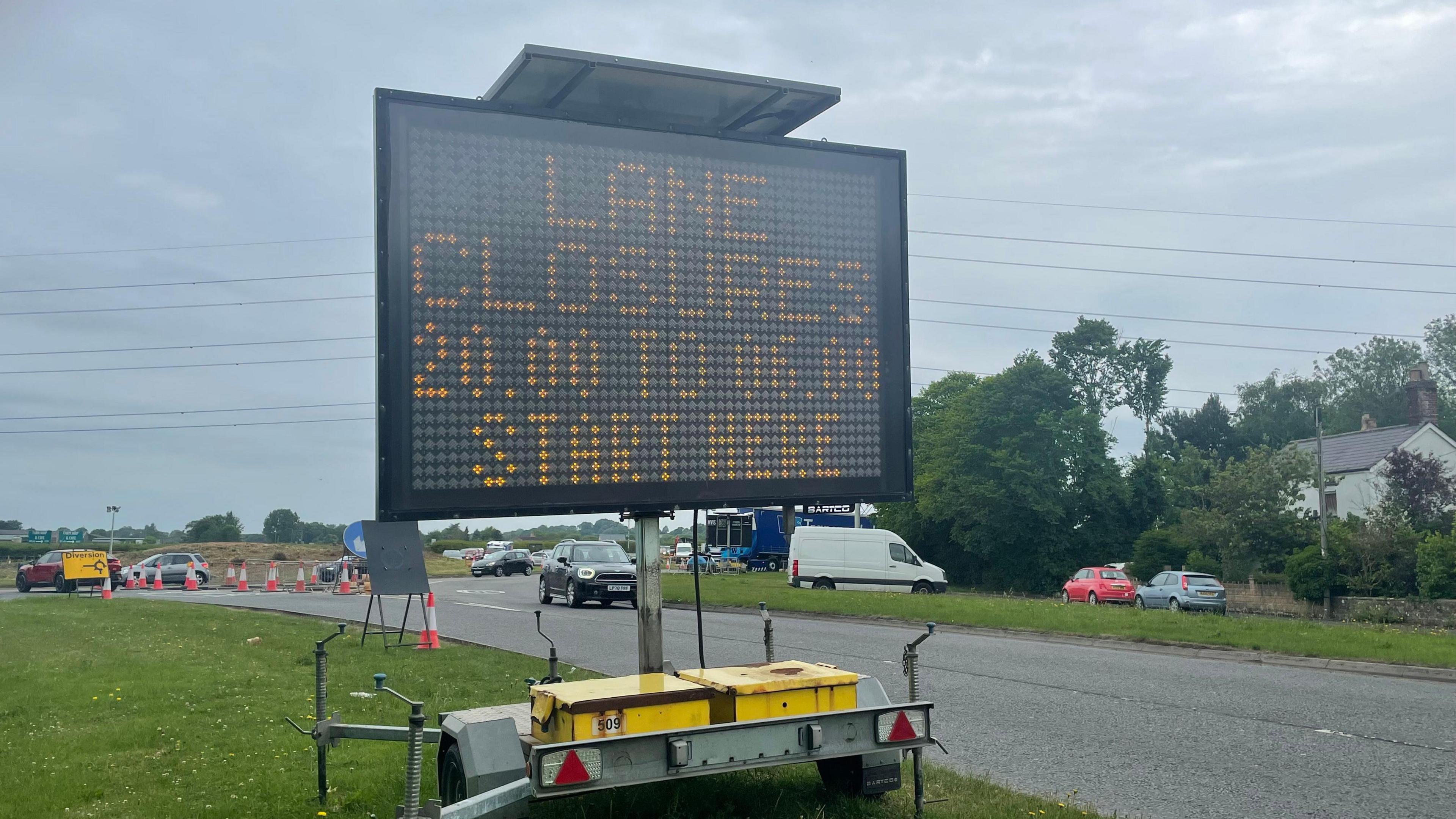 A large temporary electric sign saying 'lane closures 20:00 to 06:00 start here' standing right by a road on a very grey day