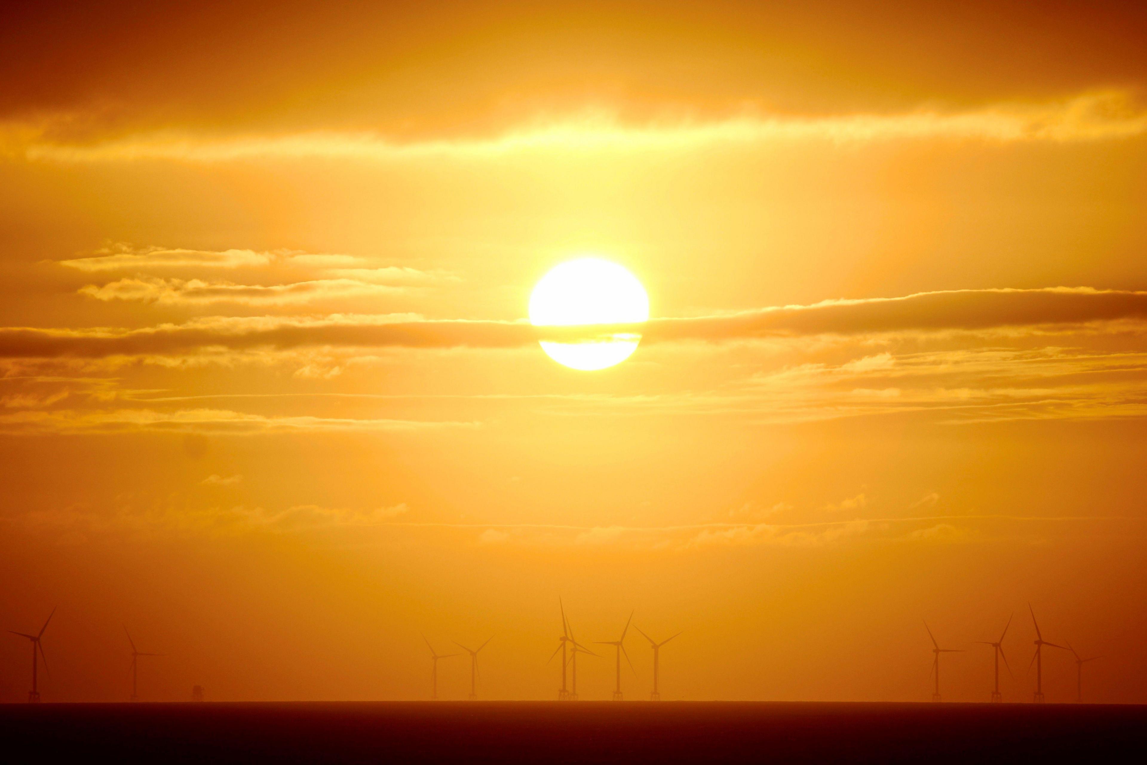 Orange and yellow sunrise, with the shapes of offshore wind turbines out at sea.