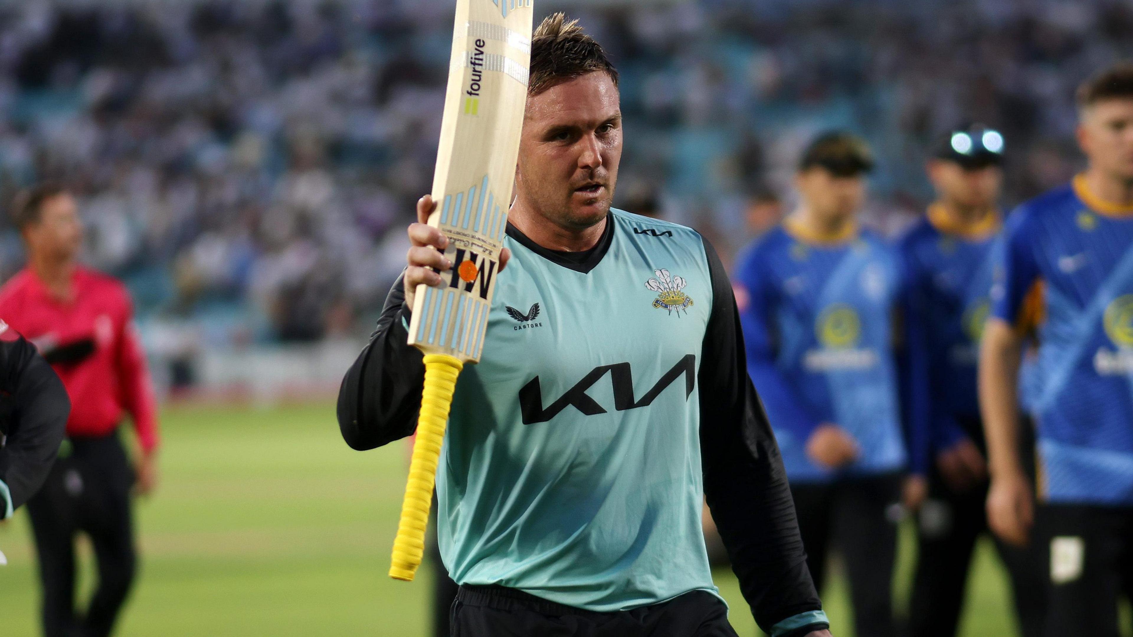 Jason Roy raises his bat to celebrate getting a century while walking off the pitch after Surrey beat Sussex