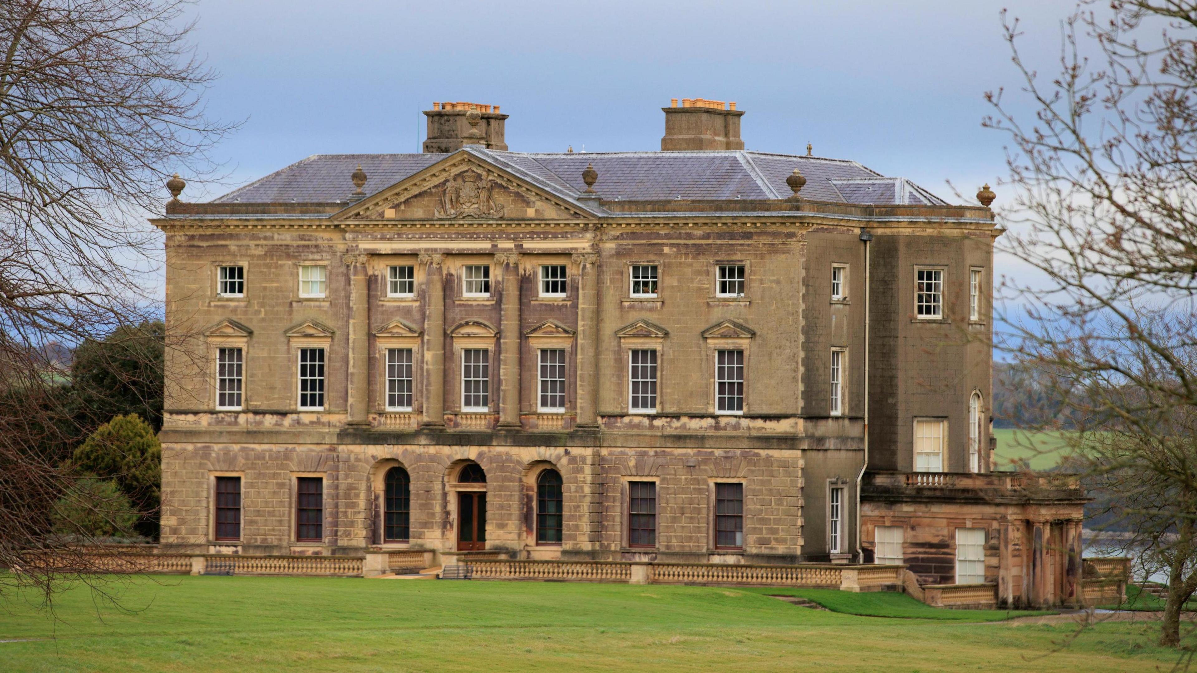 Castle Ward in County Down - an ornate 18th-century mansion overlooking Strangford Lough. The entrance side of the building is in a classical Palladian style with columns supporting a triangular pediment. A lawn stretches out in front of the building. 