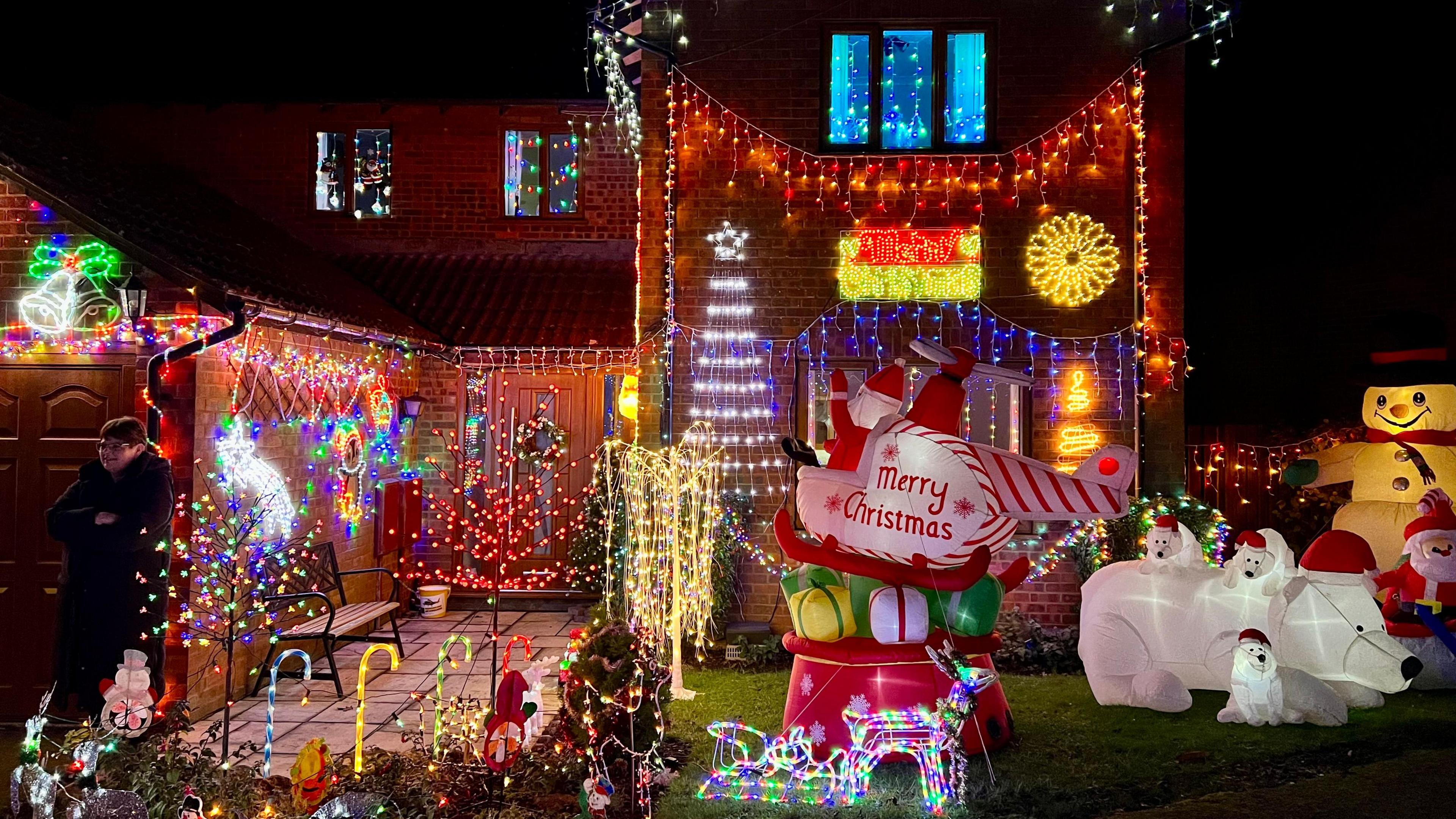 A red brick house illuminated with hundreds of different coloured lights. There are inflatable displays including a snowman and polar bears in the front garden. 