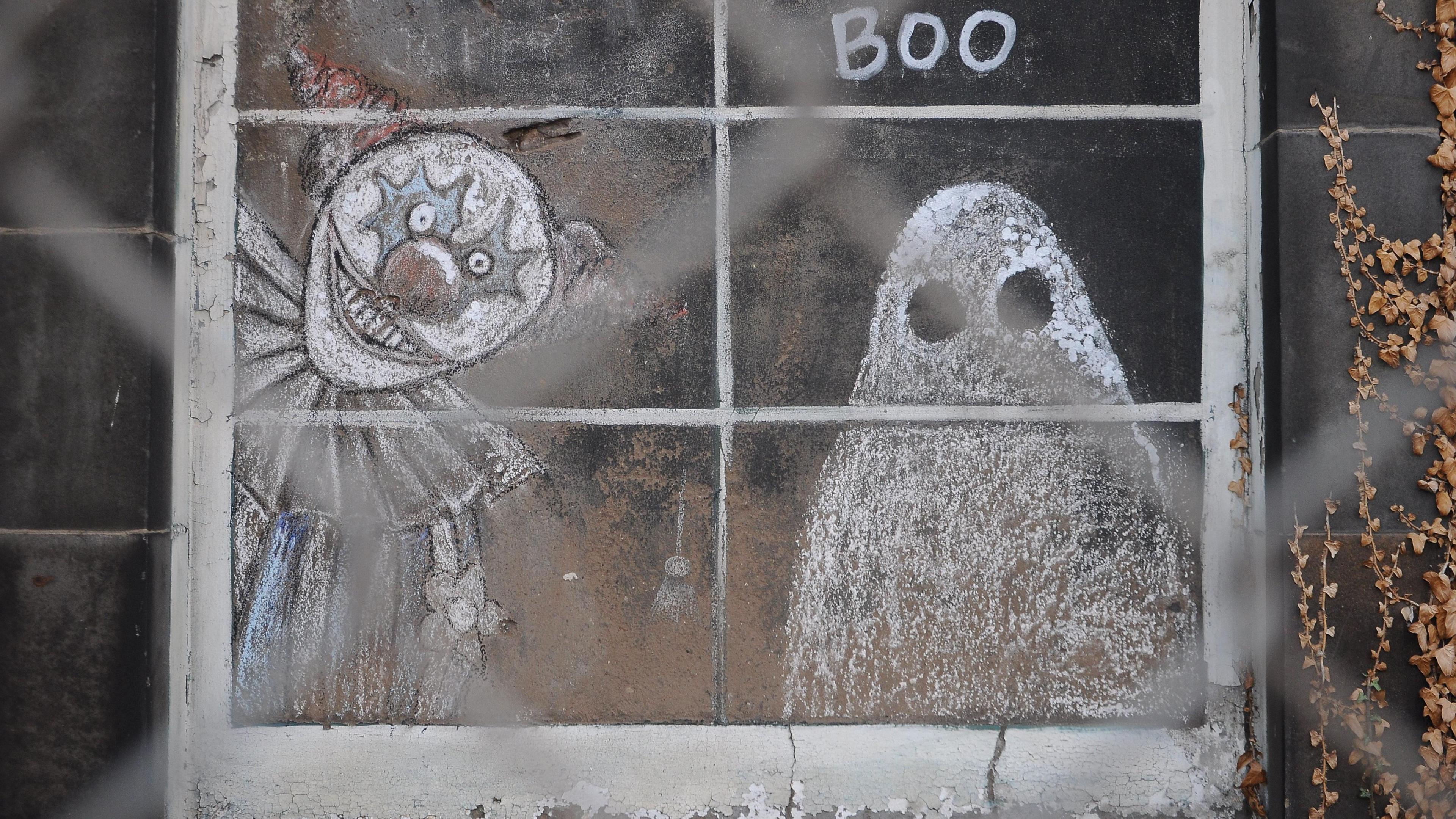 There is a clown and a ghost chalked onto a board covering a window.