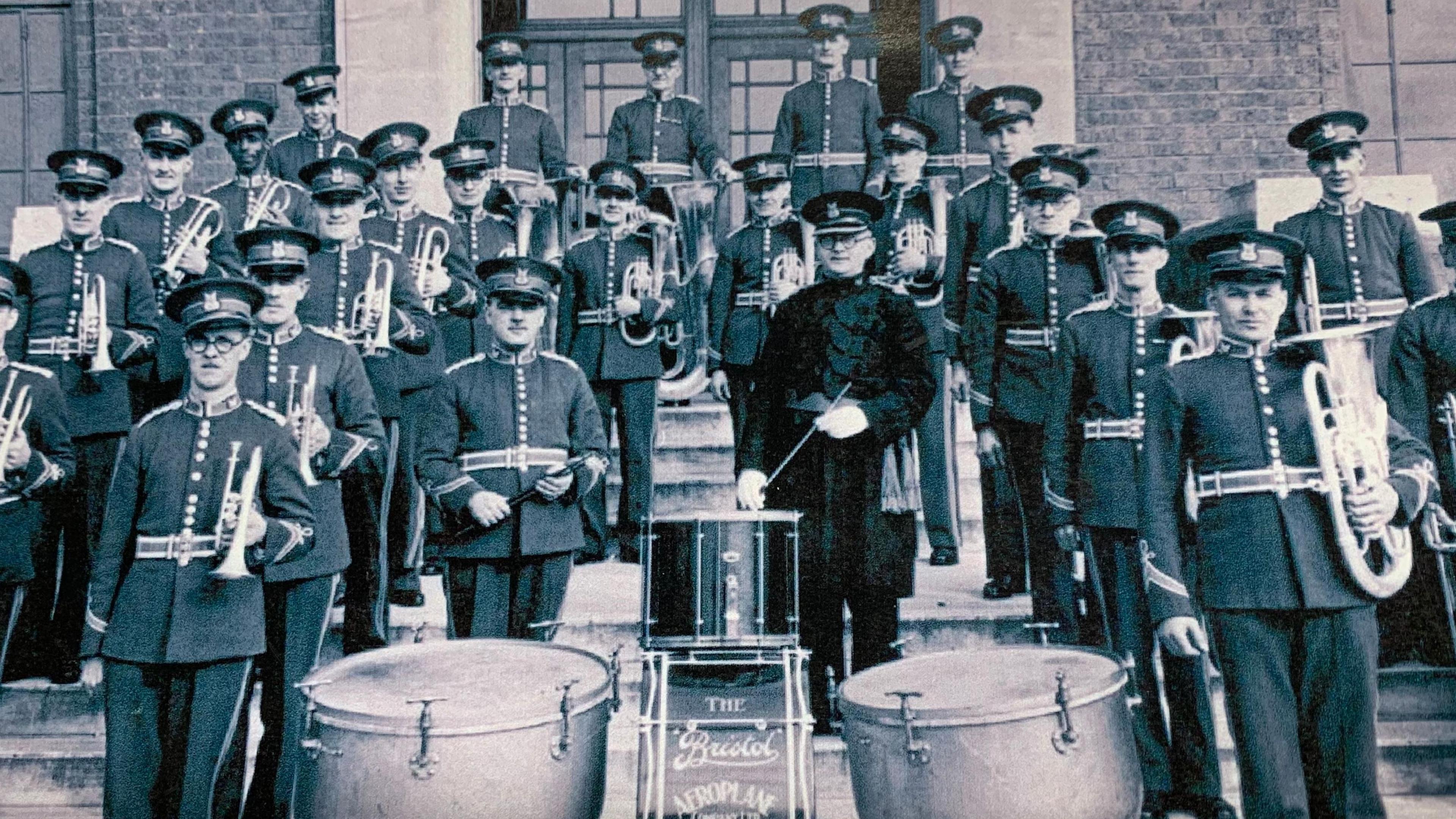 A black and white photo of the BAC Works brass band with George Yabsley in the centre in a black velvet uniform